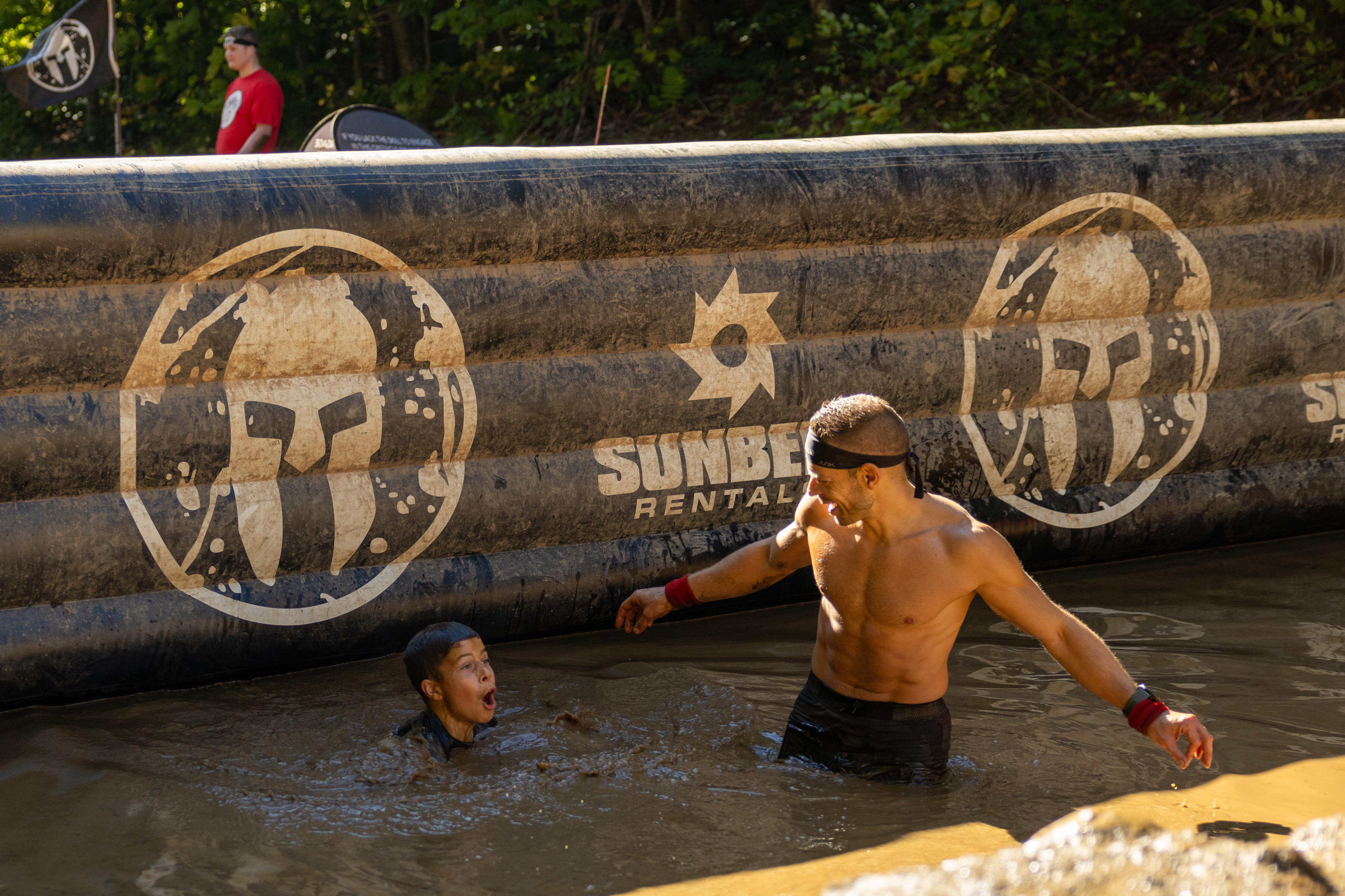 A man helps a woman in muddy water during an obstacle course event.