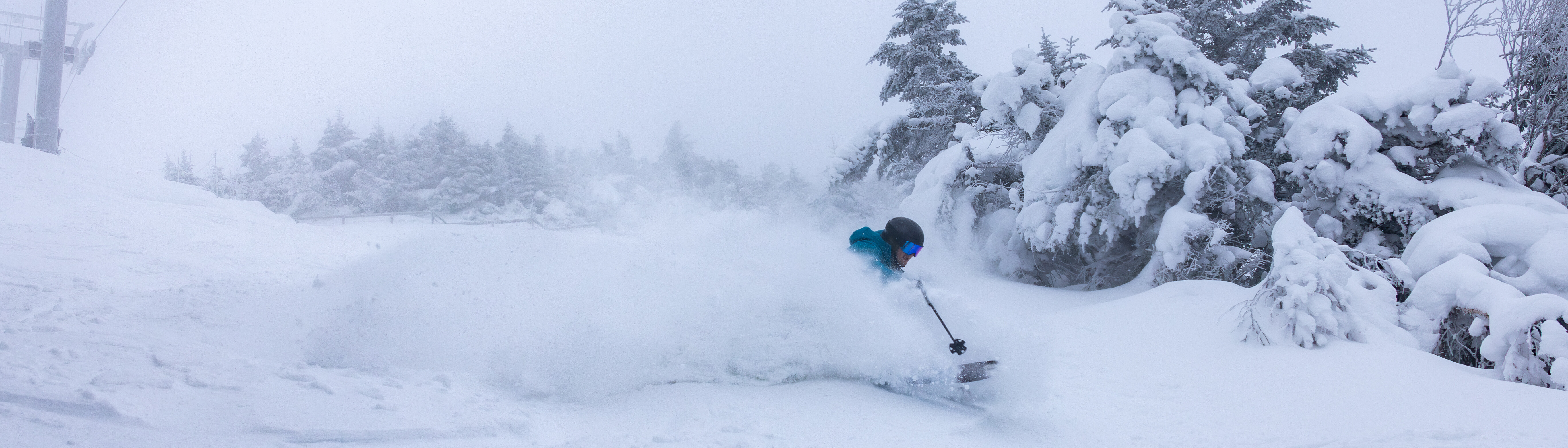 Skier carving through deep powder snow in a snowy mountain landscape.