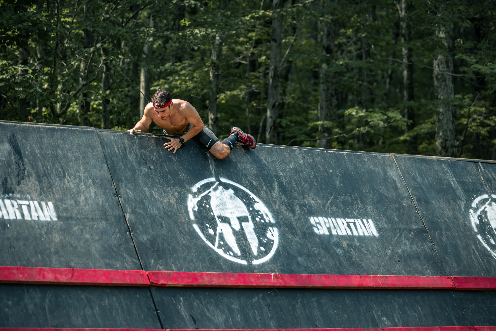 Athlete climbing an obstacle at a Spartan race in a forested area.