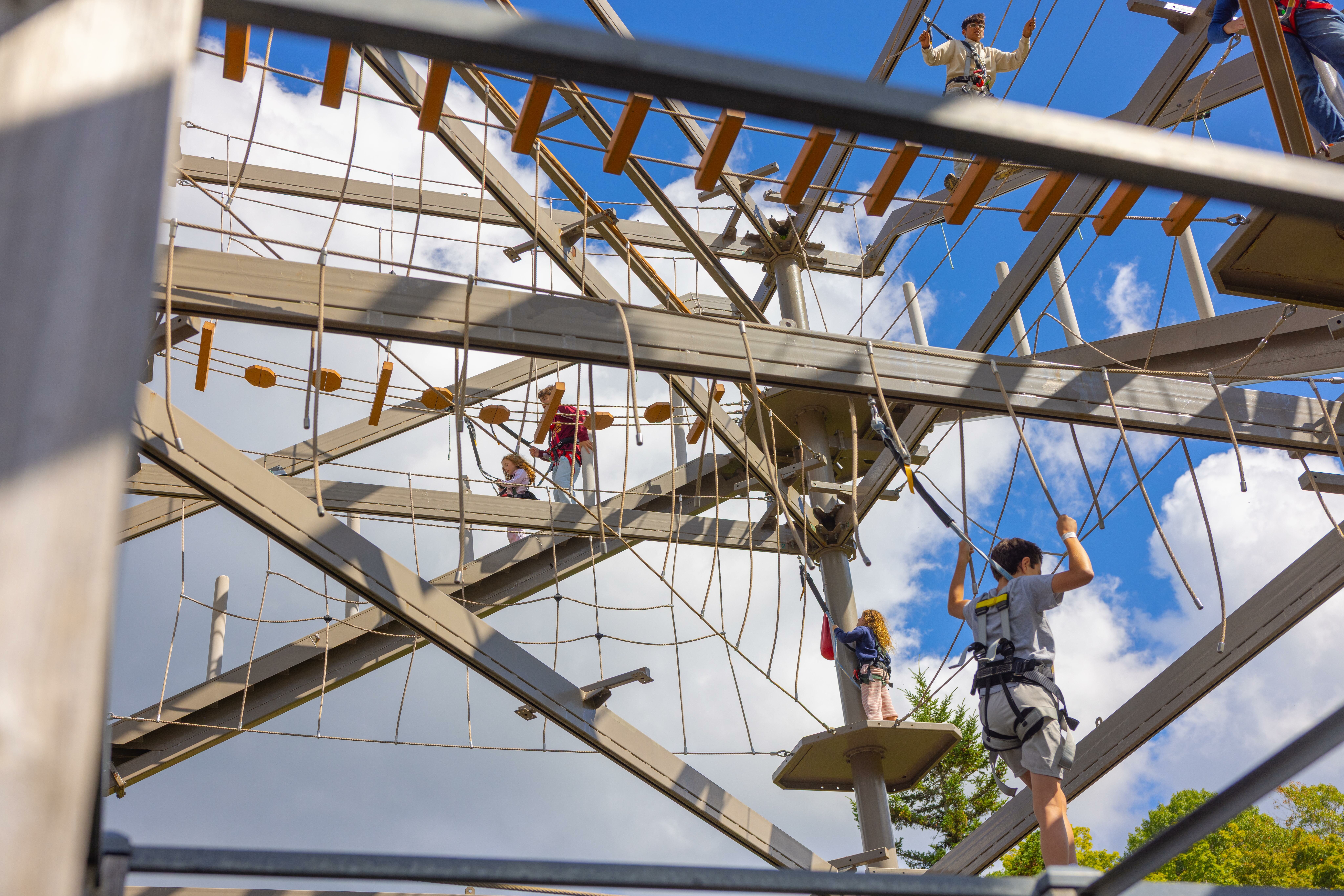 Participants navigate a high ropes course under a blue sky filled with clouds.