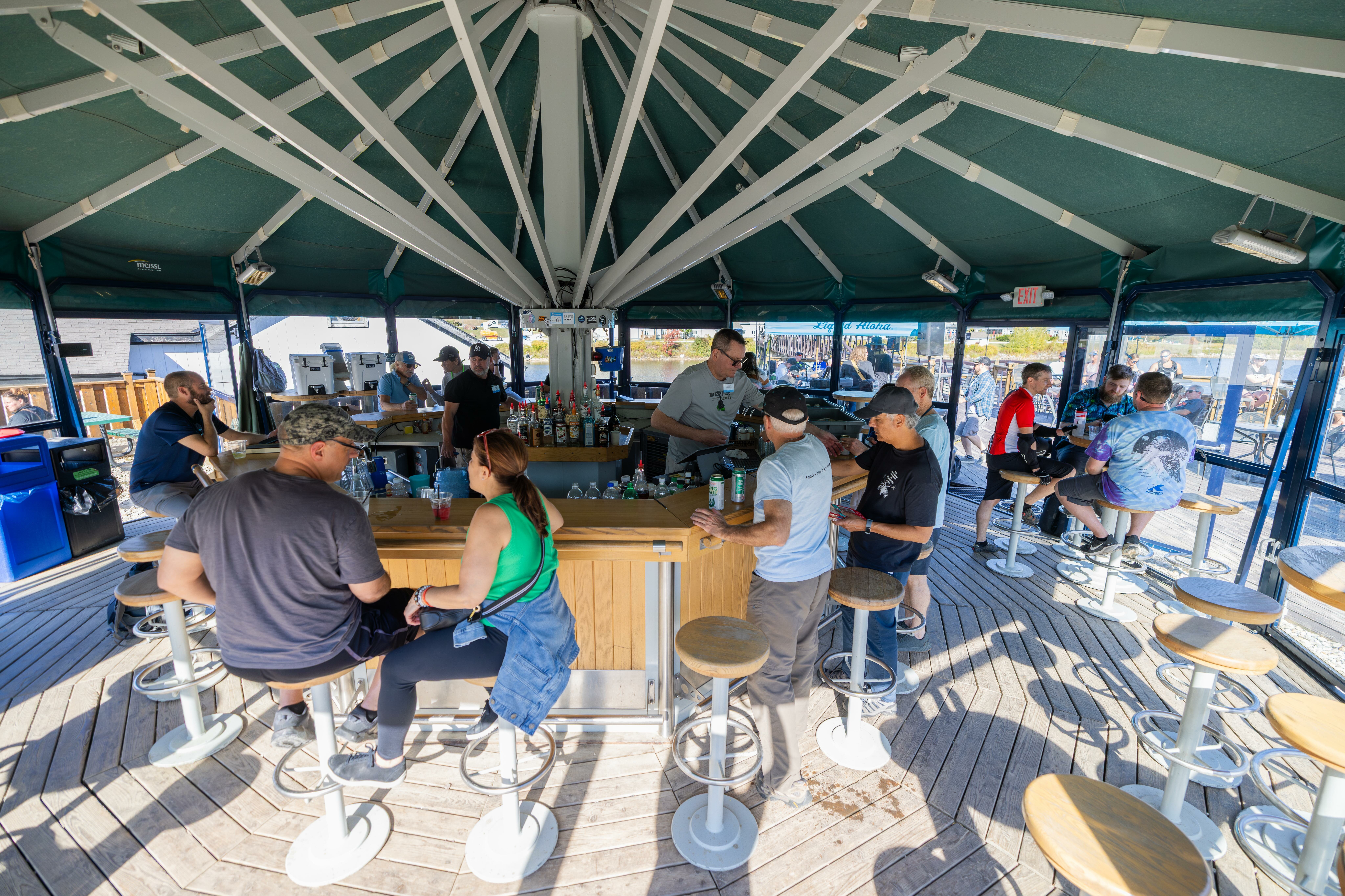 A busy outdoor bar with patrons enjoying drinks under a canopy.