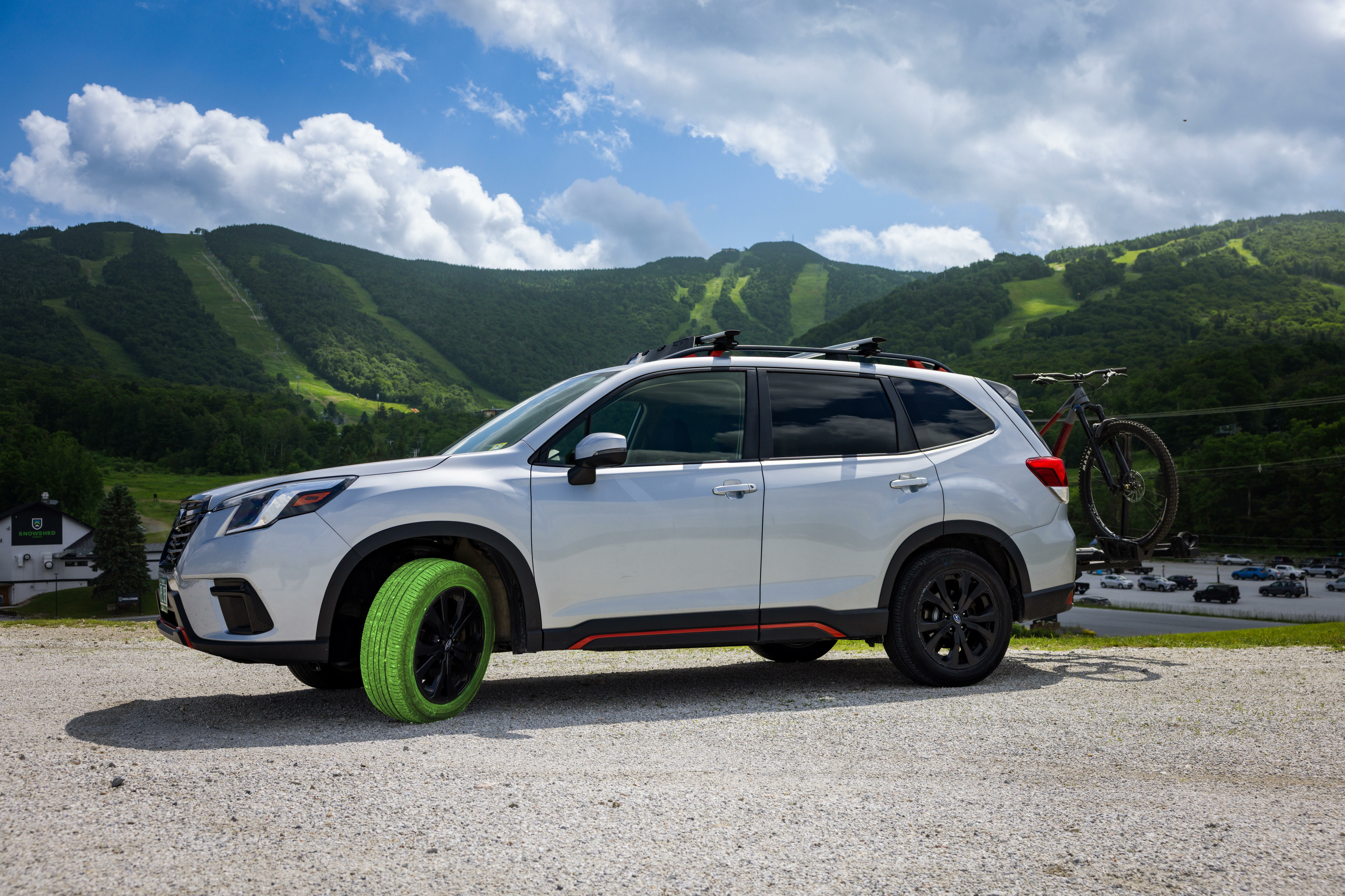 A silver Subaru with a green tire parked near mountains, bike mounted on the rear.