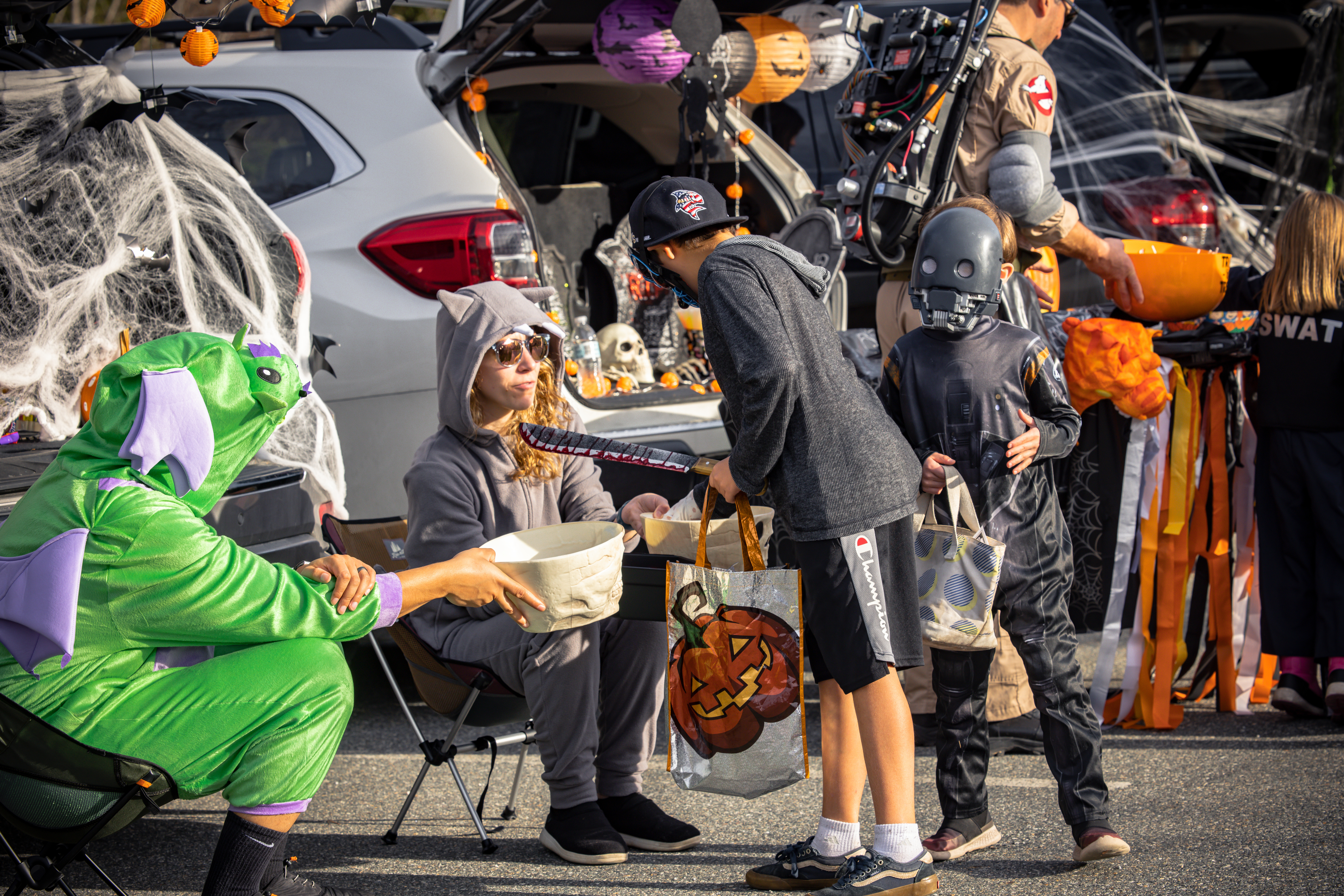 Kids in costumes trick-or-treating from a decorated car at a Halloween event.