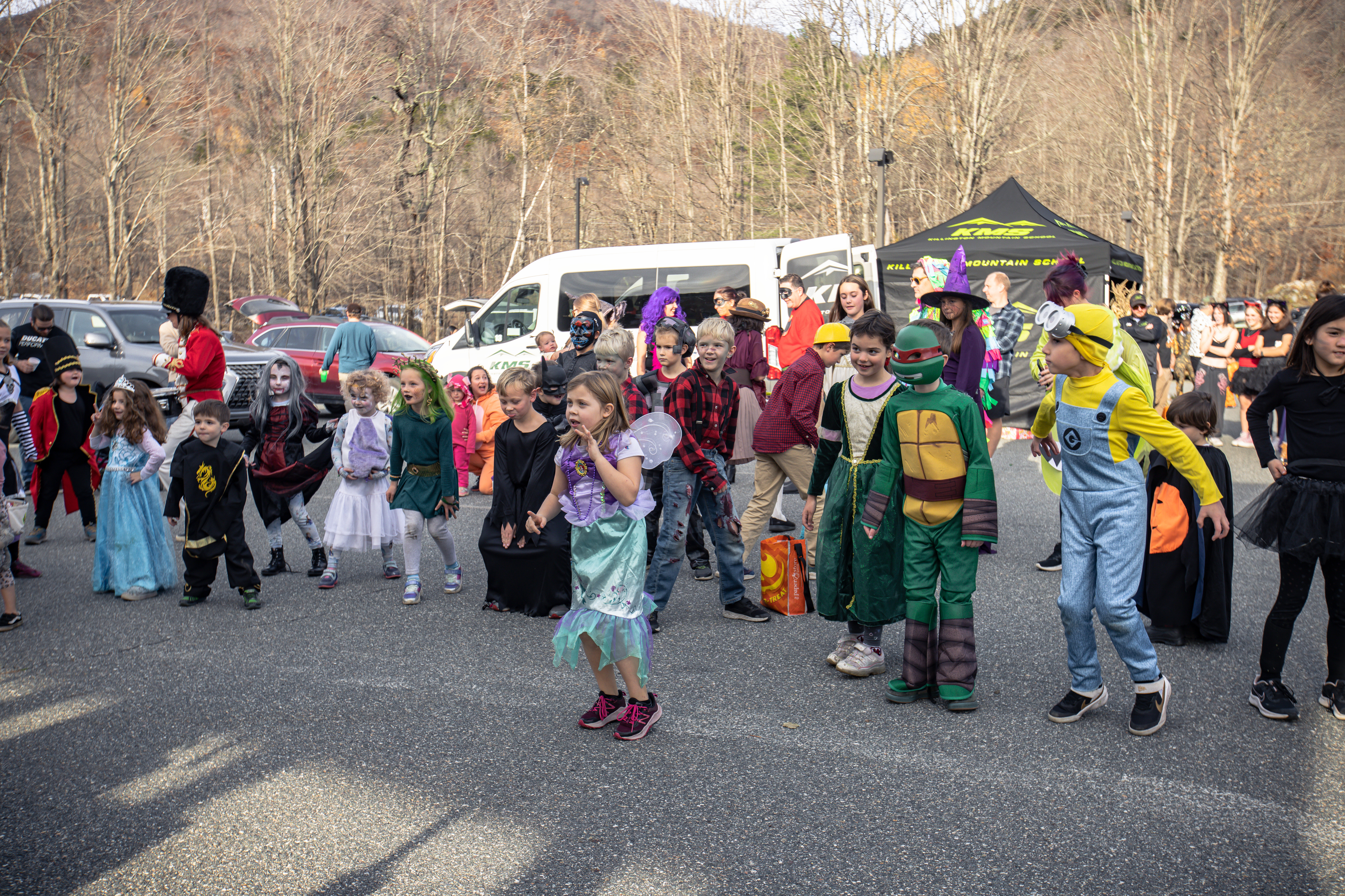 Children in costumes dance and play together at an outdoor Halloween event.