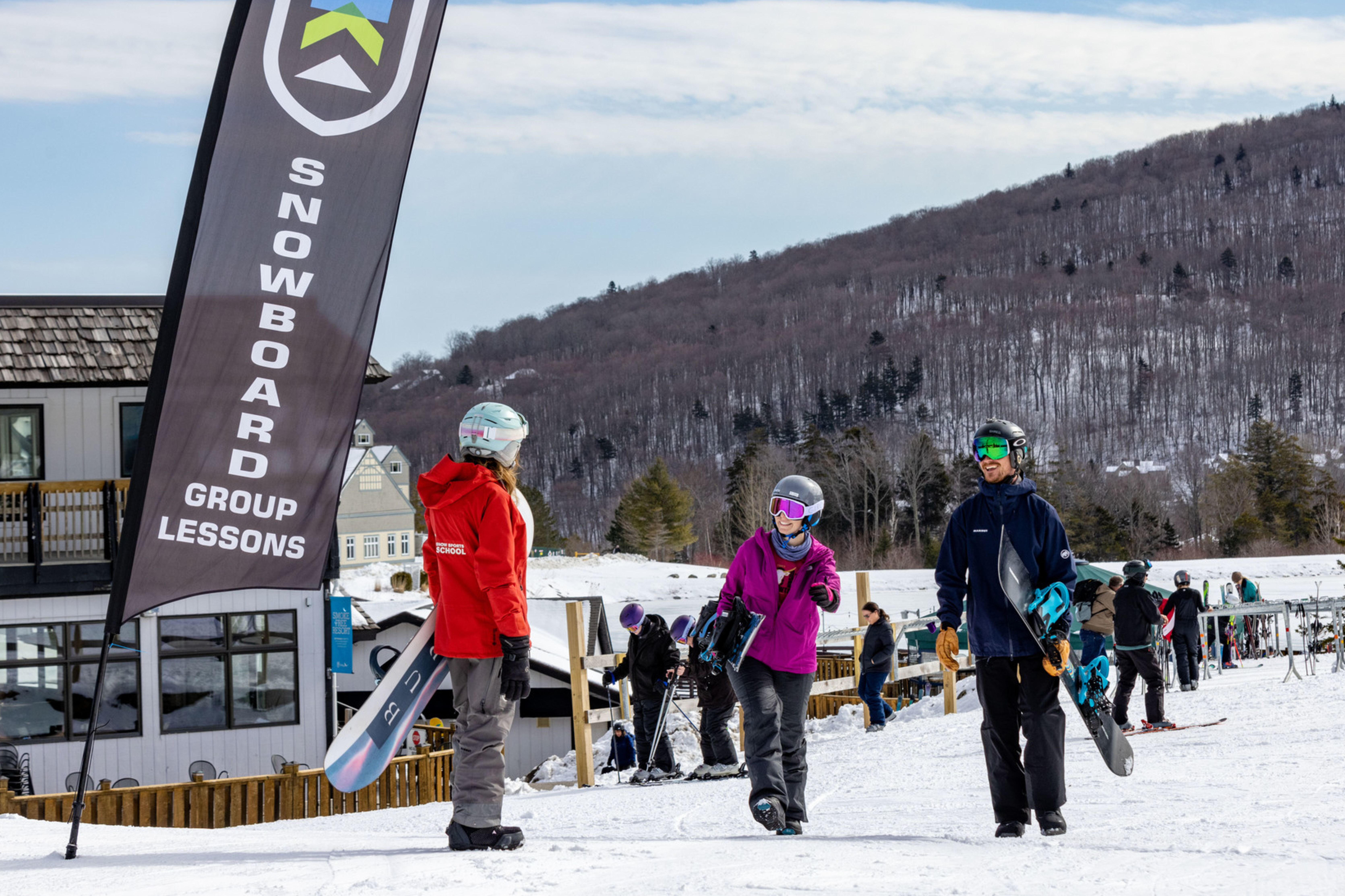 Group of snowboarders chatting near a lesson sign on a snowy mountain.