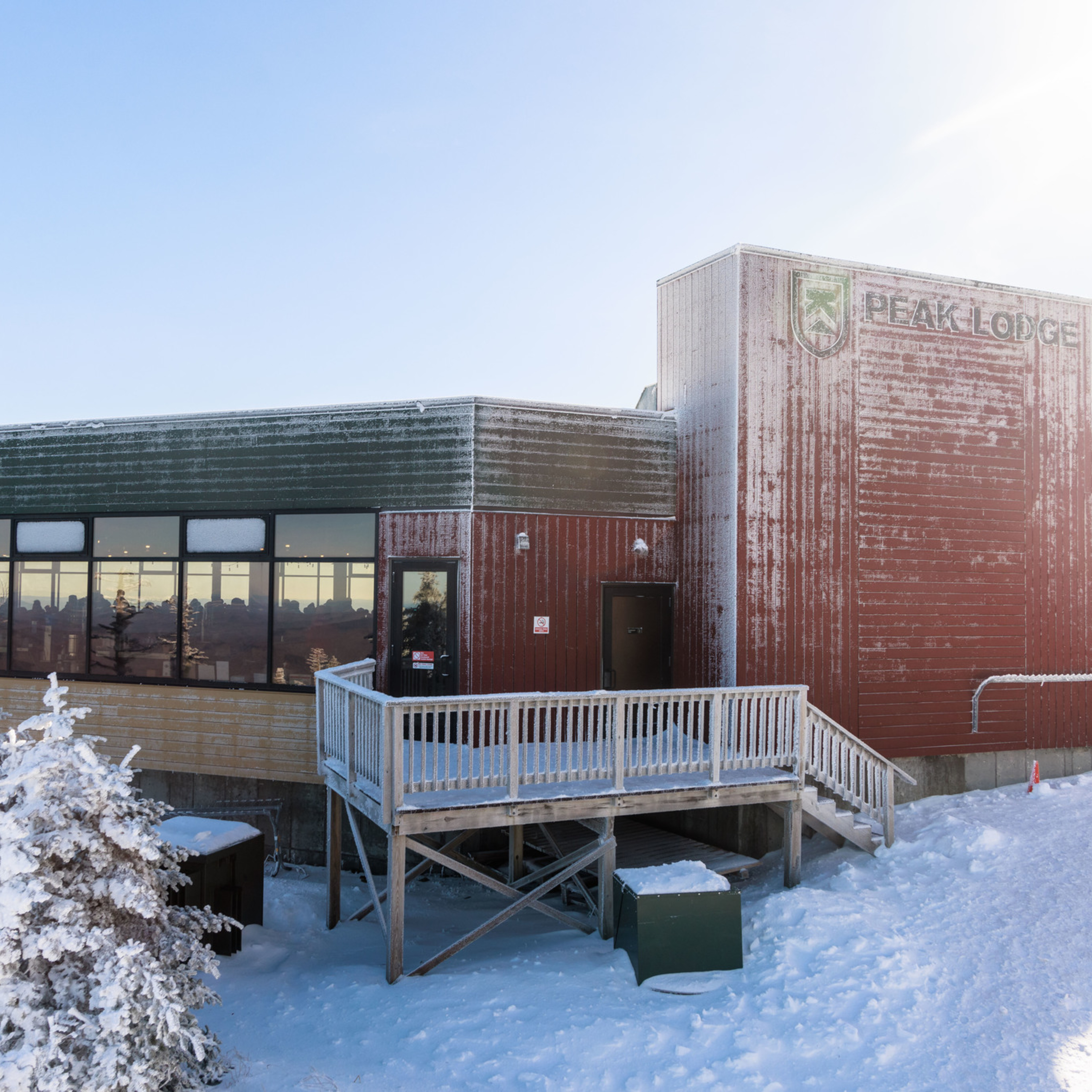 Snow-covered Peak Lodge with a wooden deck and frosted windows under a blue sky.
