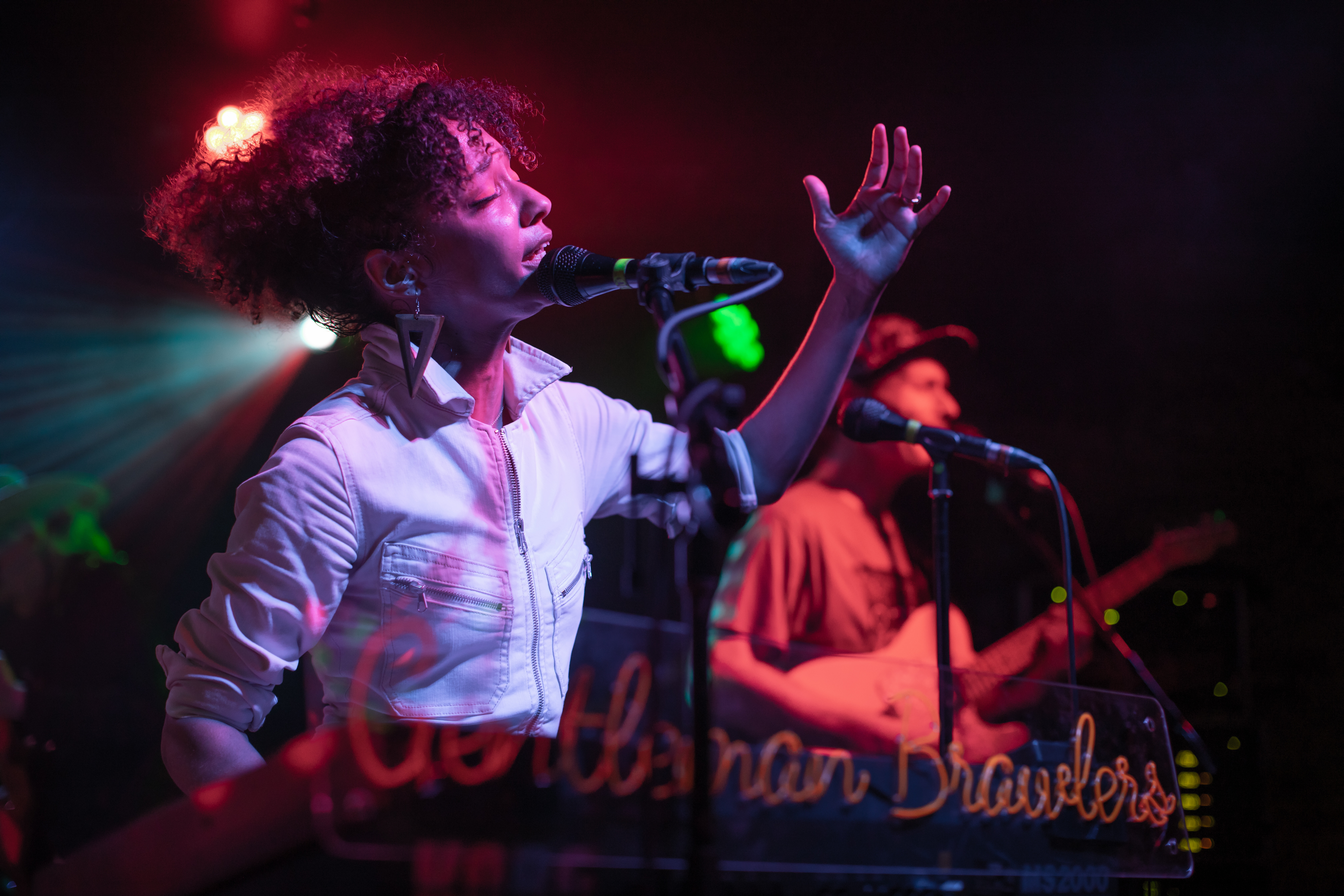 A singer passionately performs on stage with a band, surrounded by colorful stage lights.
