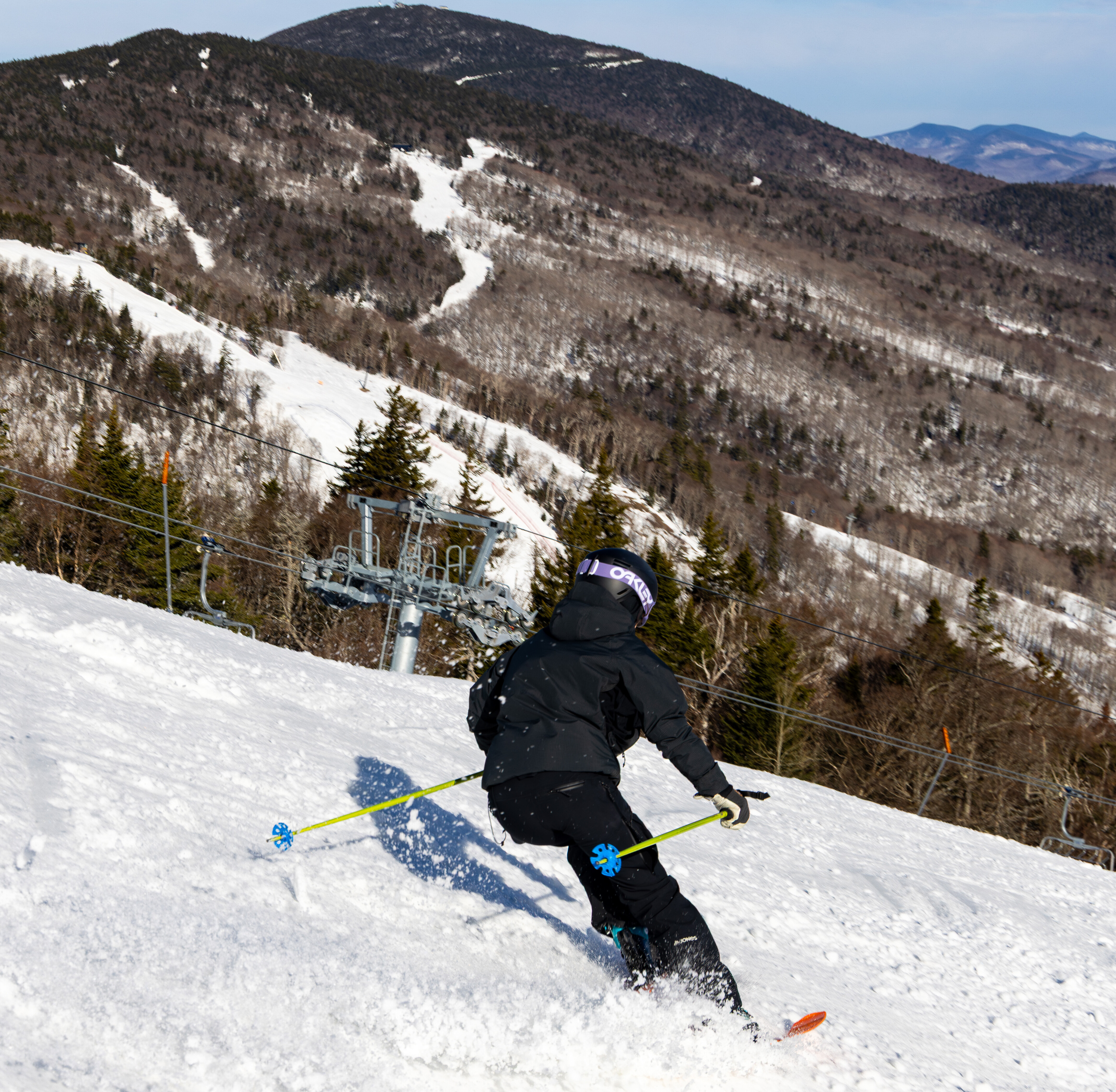 Skier in black gear descends snowy slope with mountains in the background.