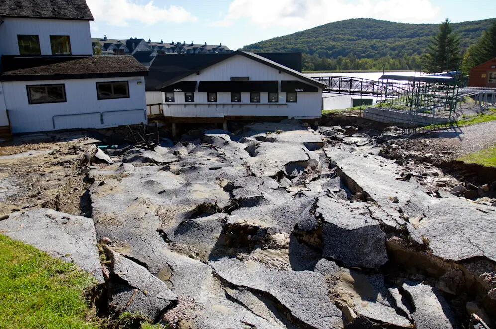 Damaged asphalt around a building, showing cracks and upheaval from ground movement.