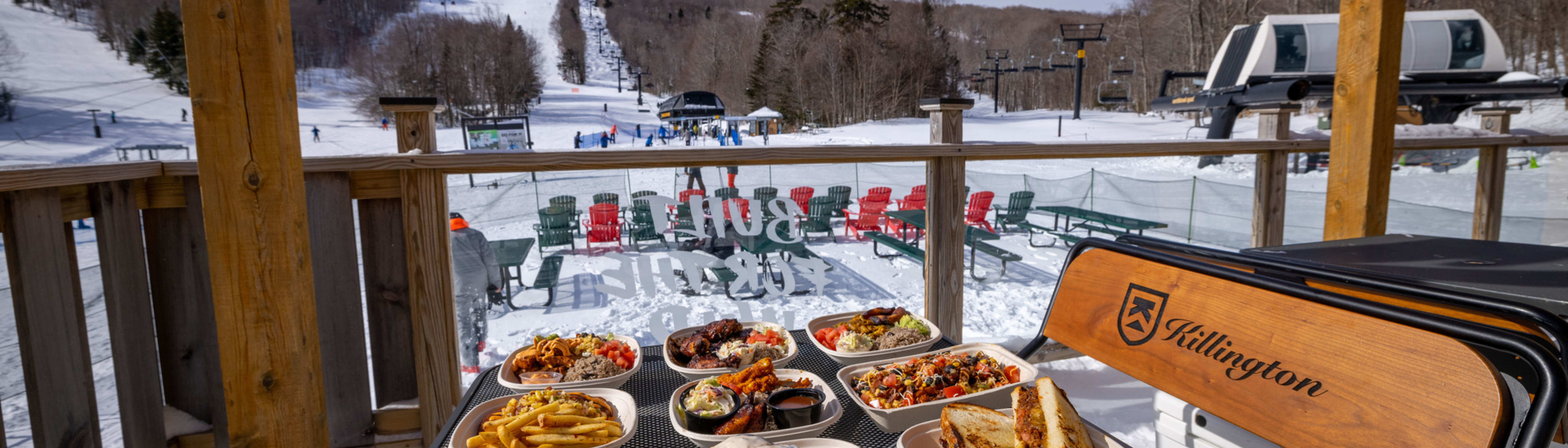 A table of diverse dishes overlooks a snowy ski resort.