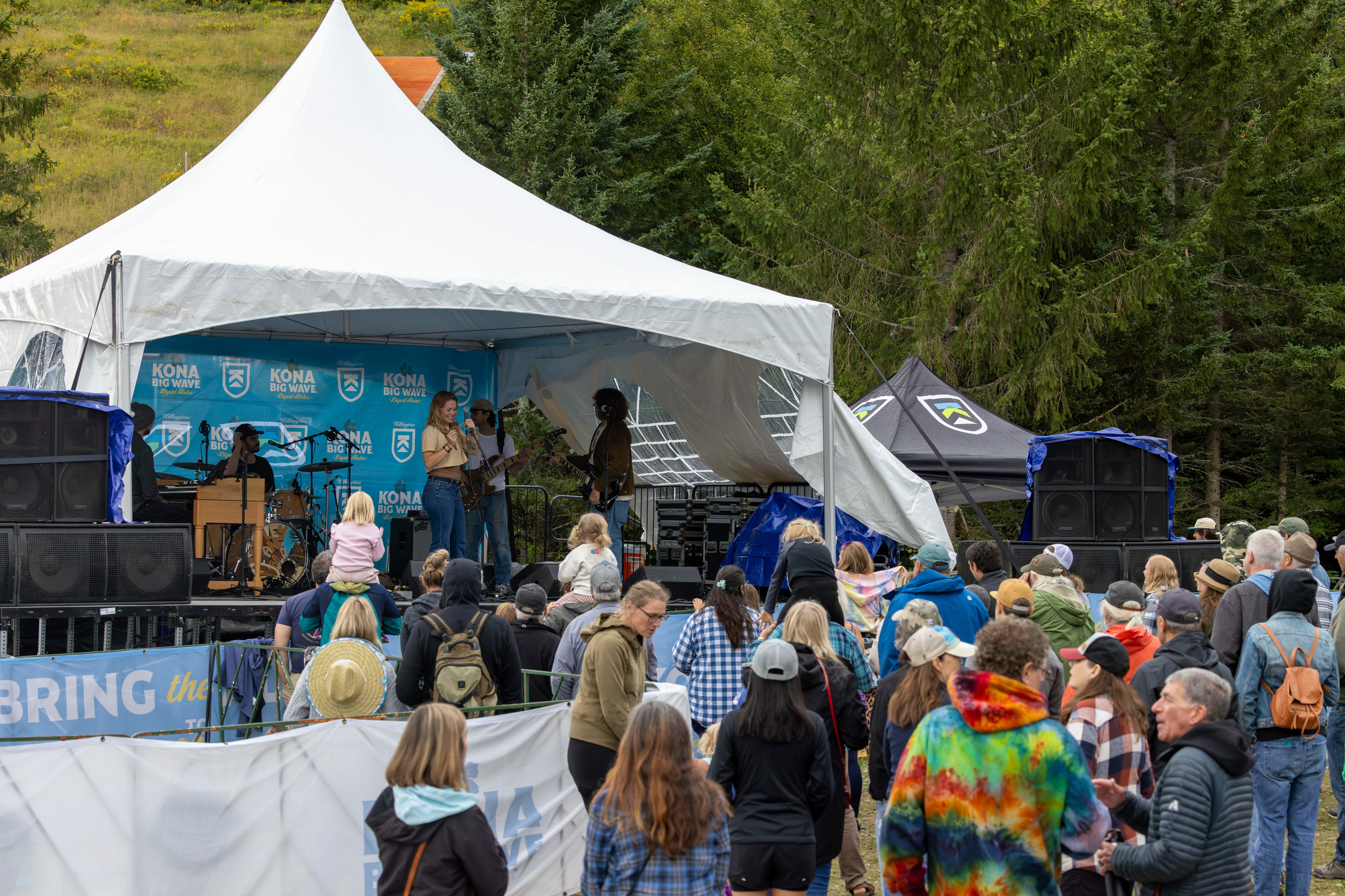 Live band performing on stage with an audience enjoying the music outdoors.