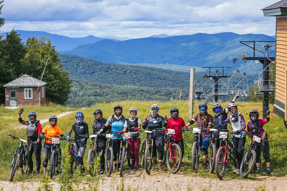 Group of mountain bikers posing on a hillside with mountains in the background.