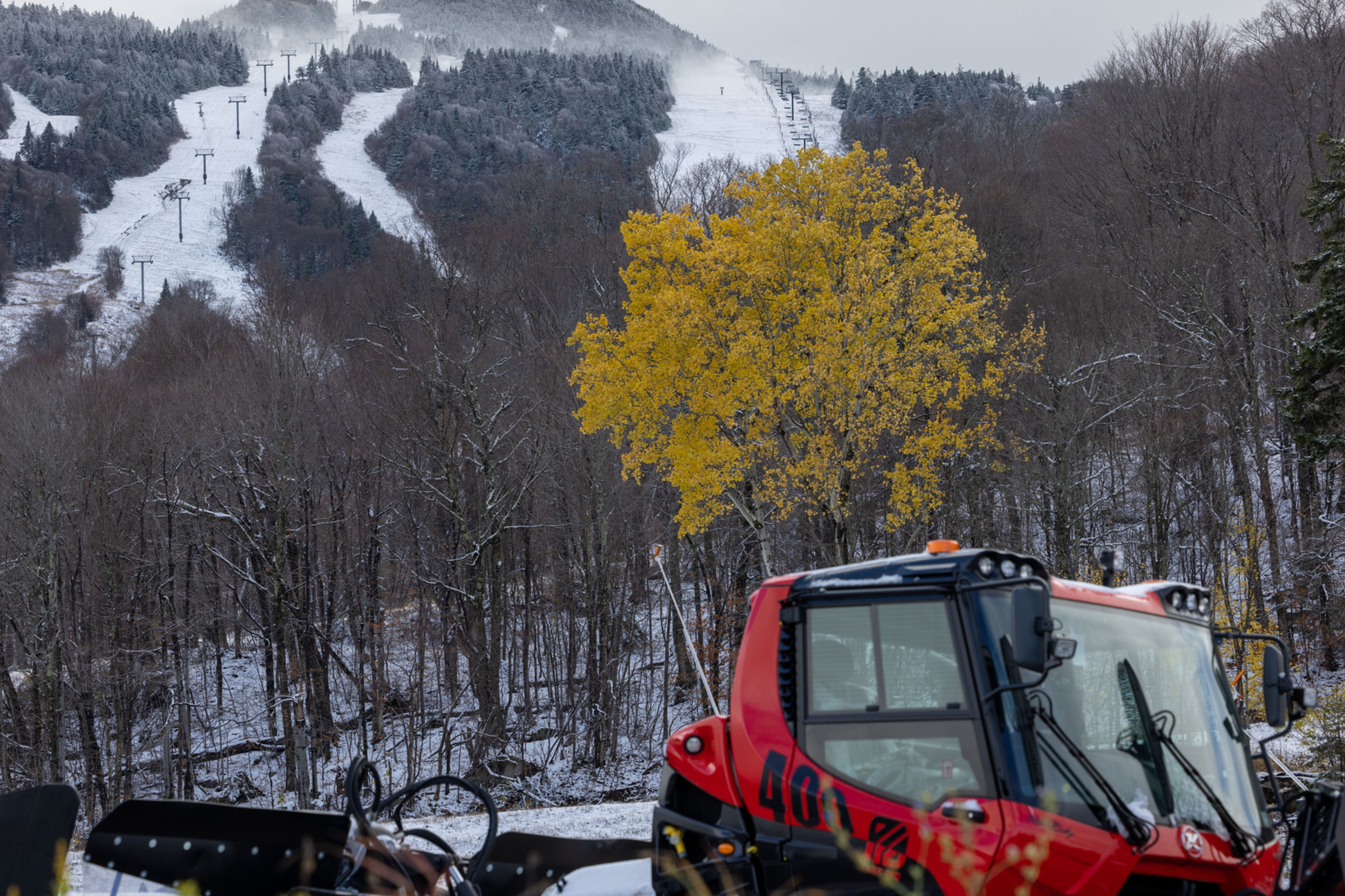Bright yellow tree in foreground, snowy ski slopes and machinery in the background.