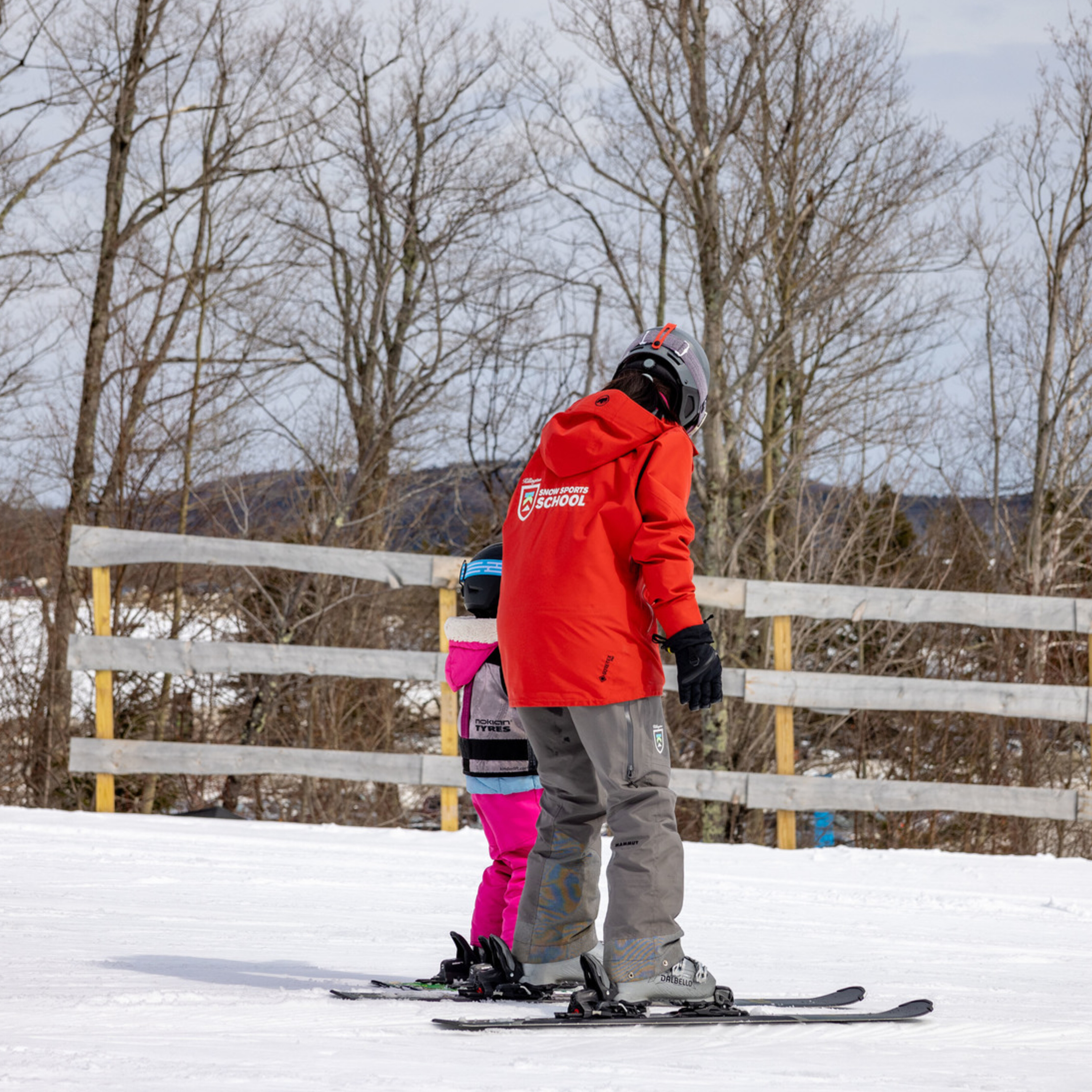 Ski instructor teaching a child on snowy slopes with trees in the background.
