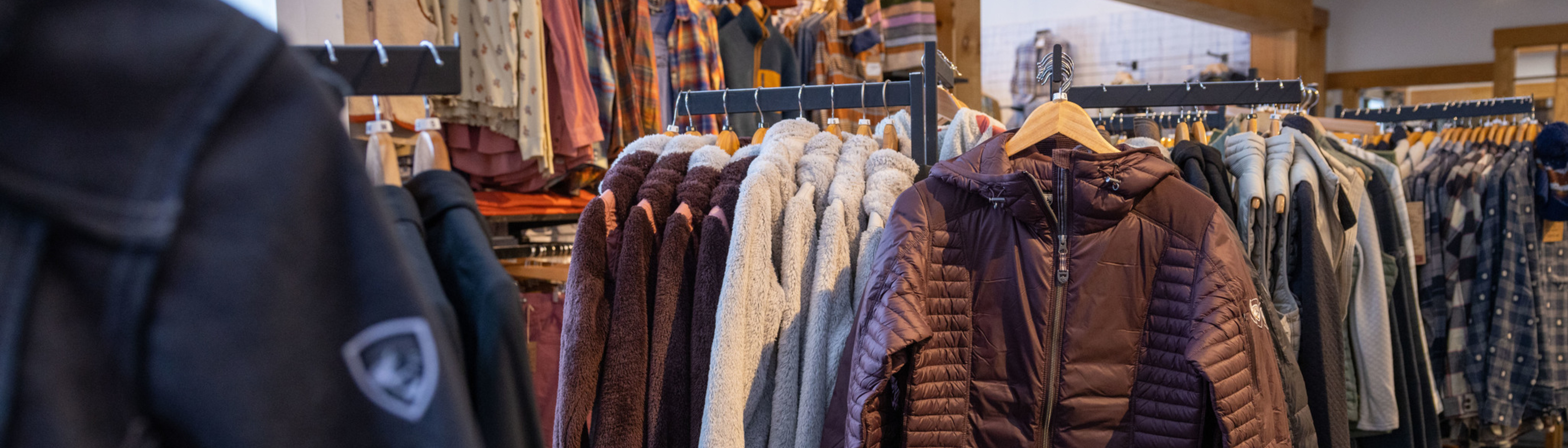 Clothing racks display various jackets and sweaters in a retail store.
