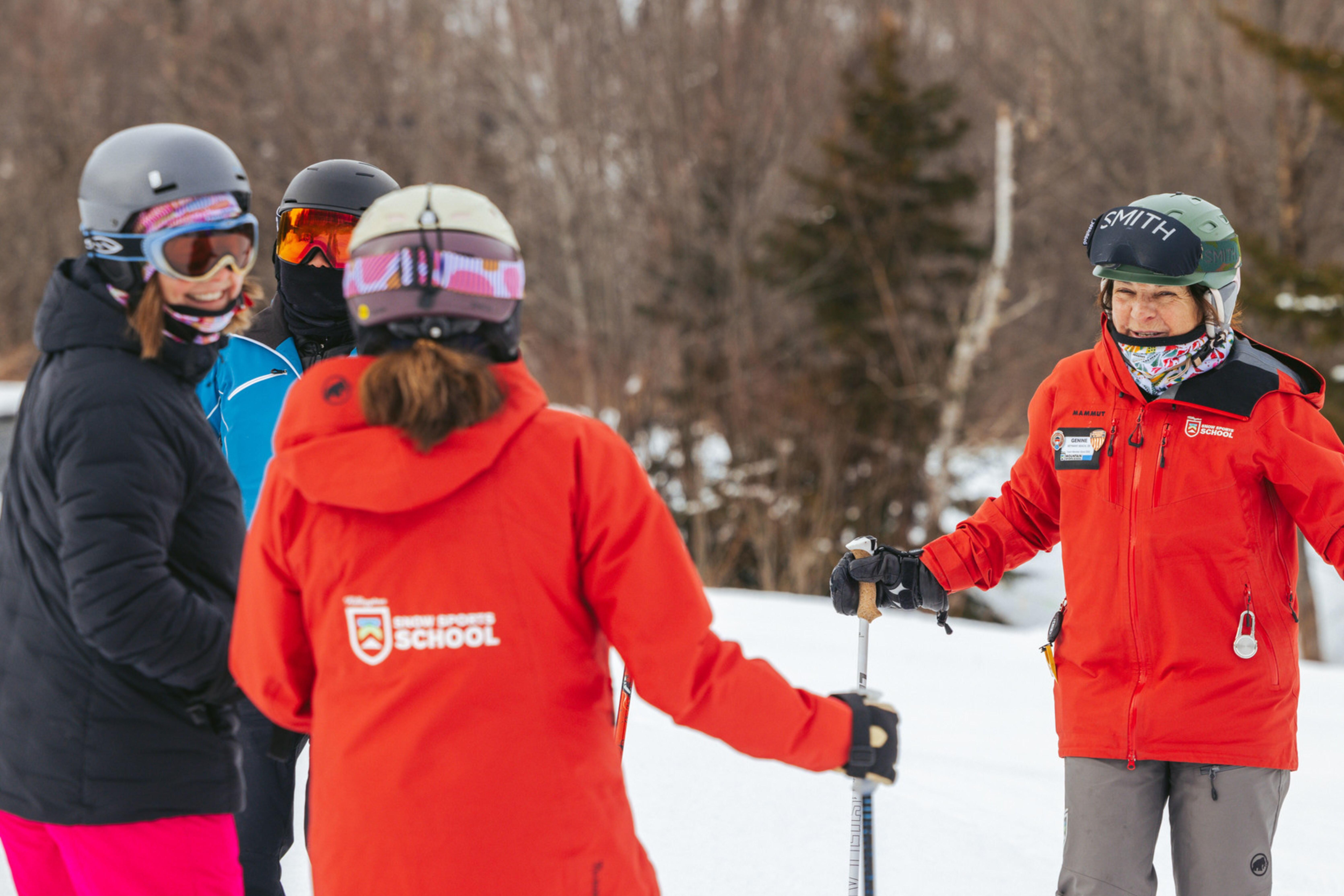 Group of skiers chatting on the slopes, with an instructor in red gear.