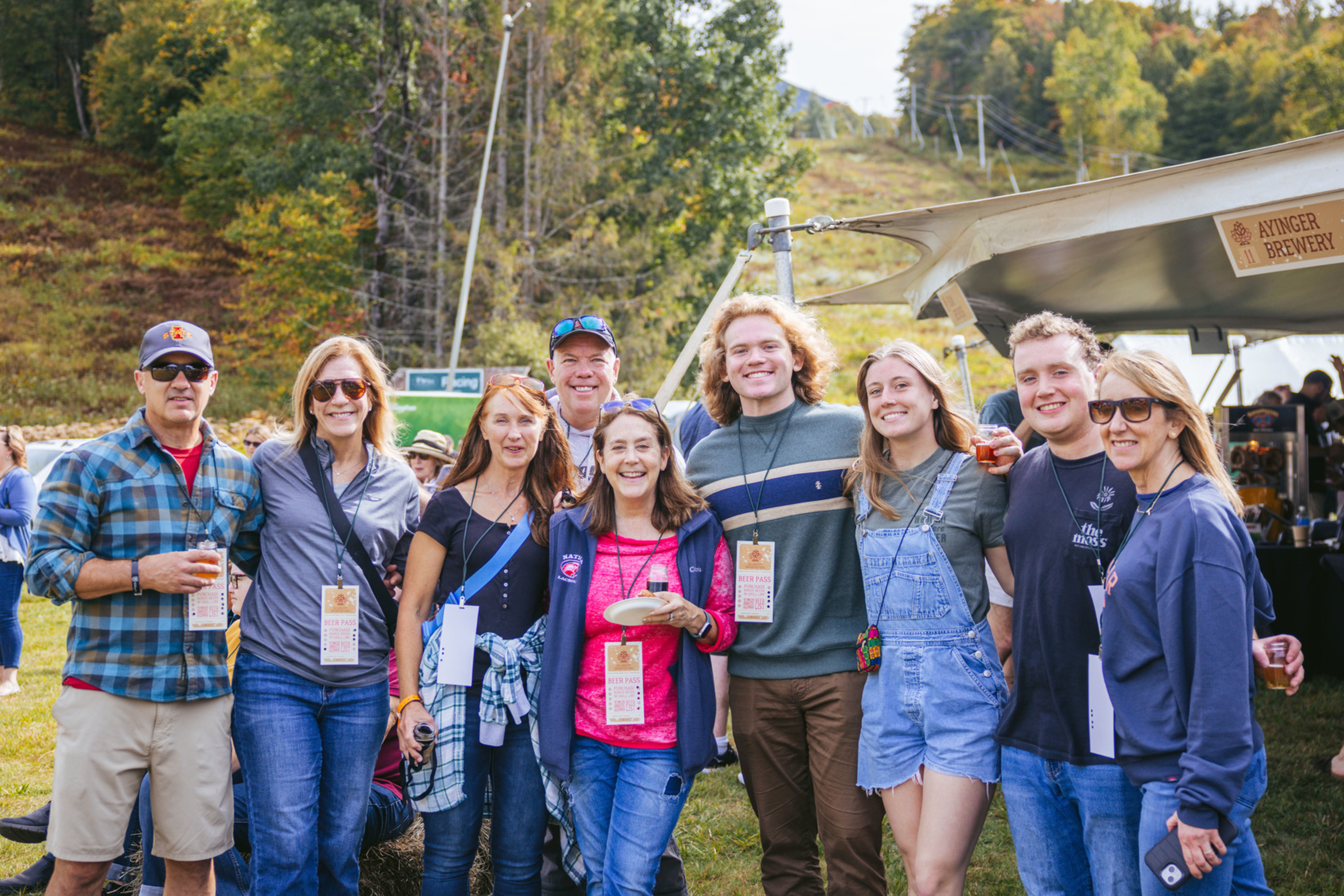 Group of eight people enjoying a festival outdoors, smiling and holding drinks.