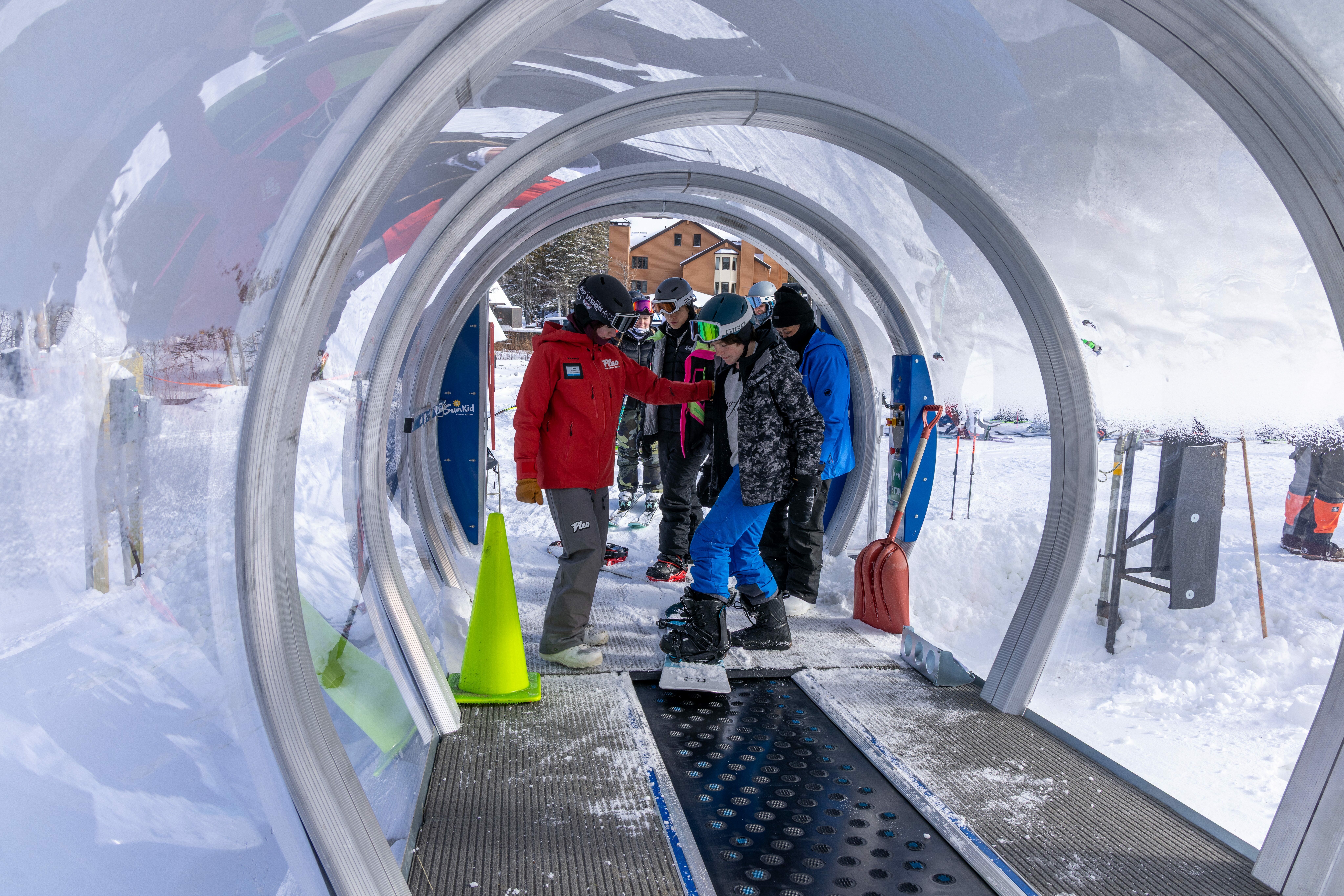 Skiers and an instructor navigate a snowy tube entrance at a ski resort.
