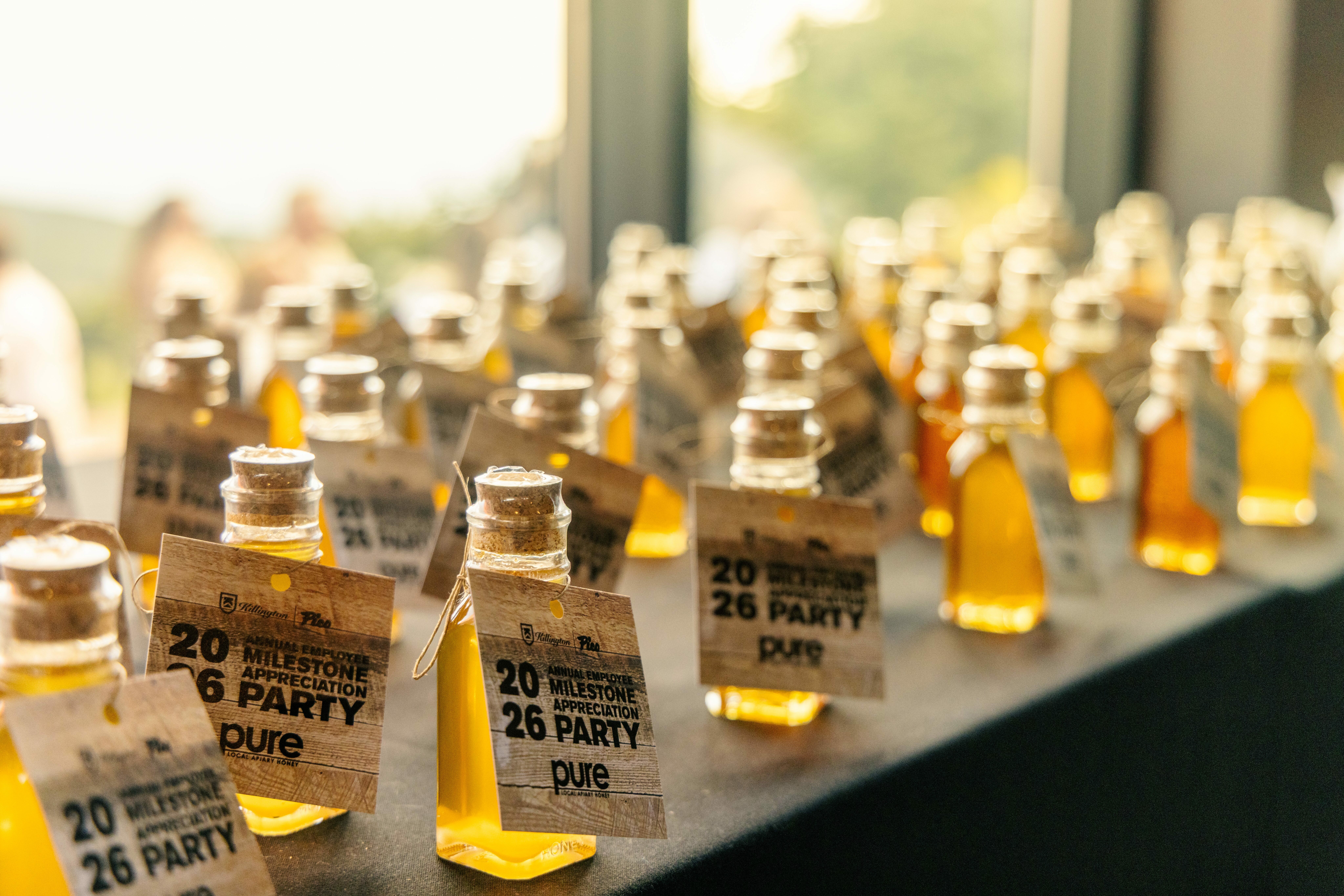 Tables lined with small bottles of honey labeled for a milestone appreciation party