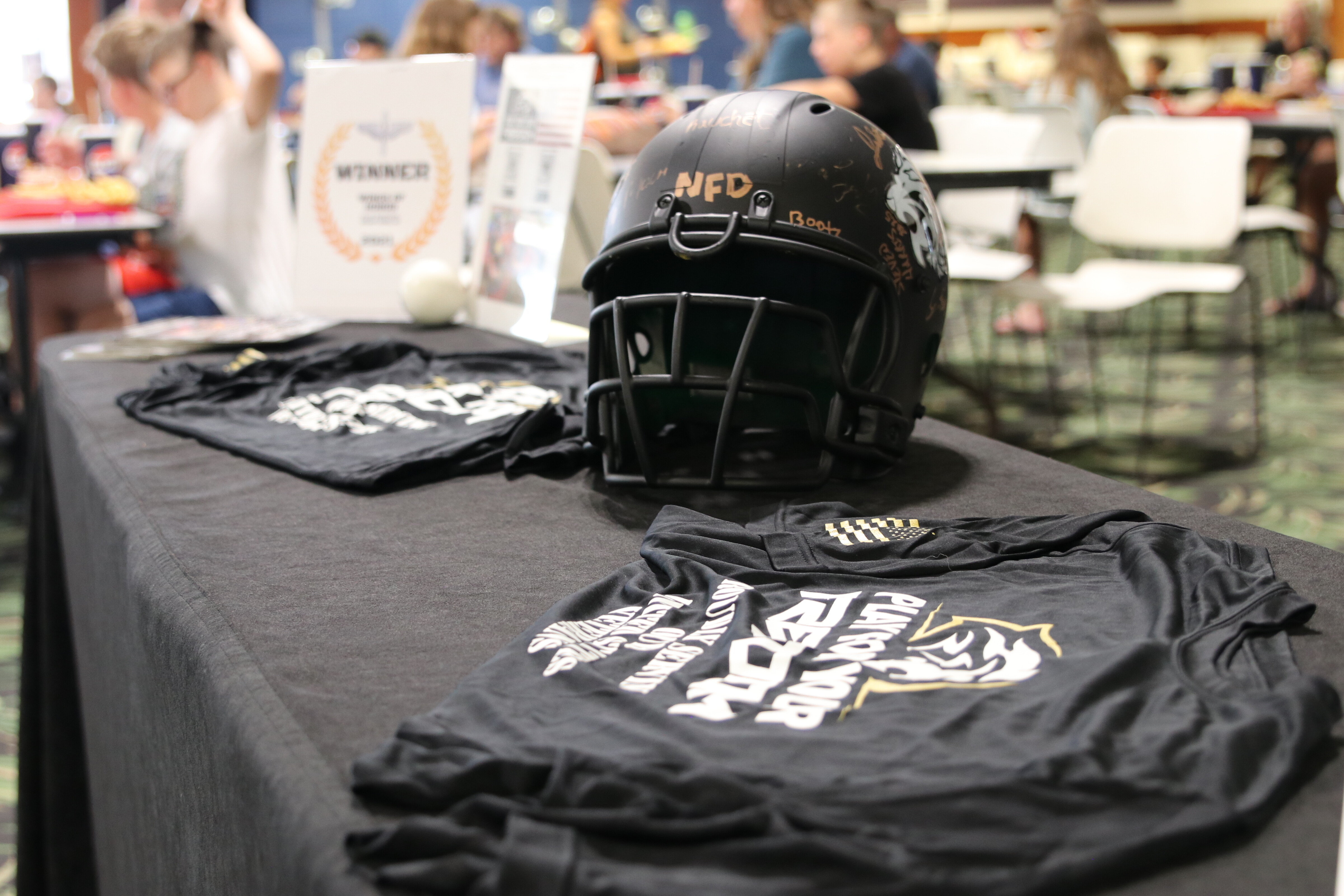 A football helmet and black t-shirts displayed on a table at an event.
