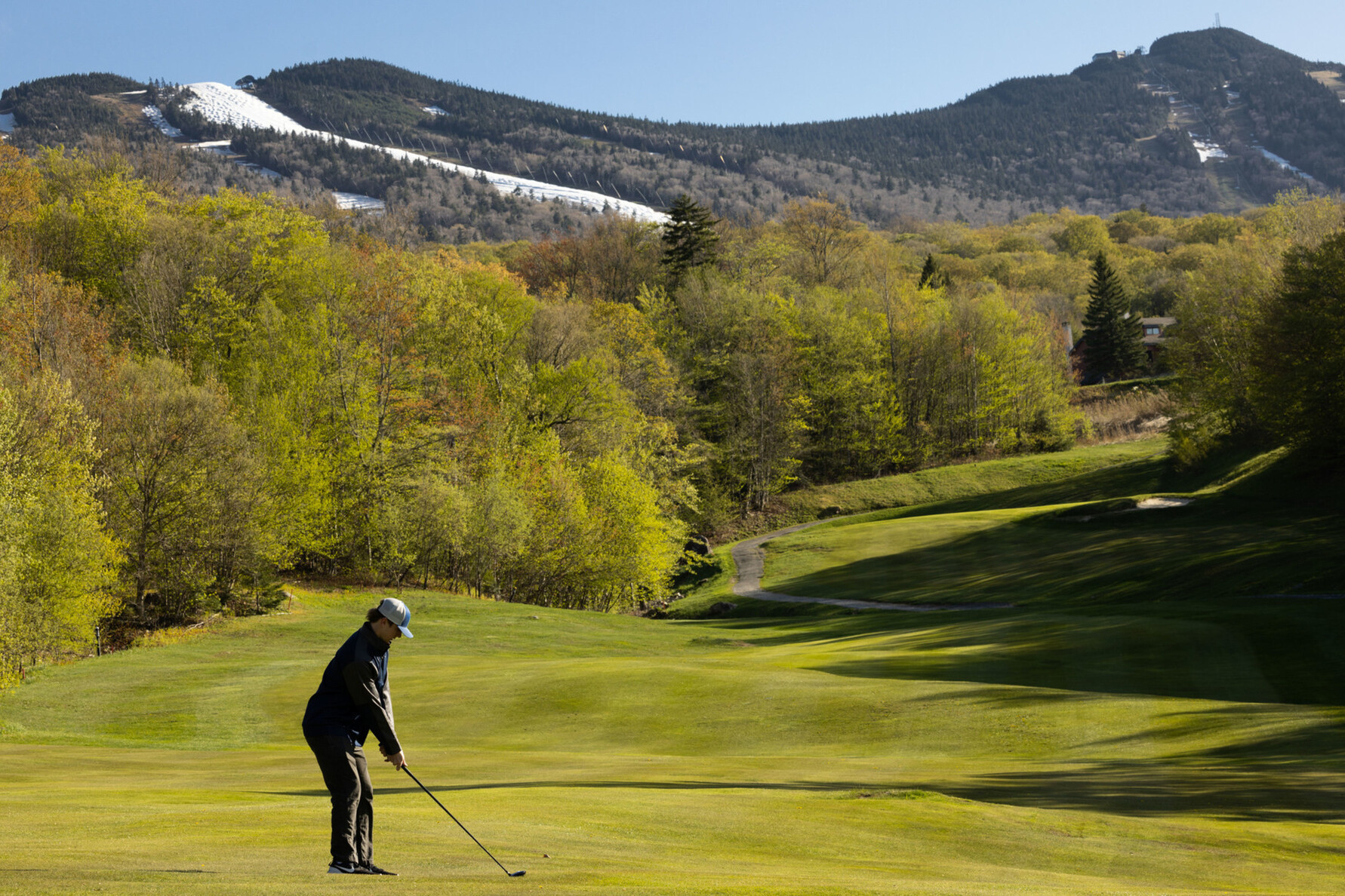 Golfer preparing to swing on a green course with snowy mountains in the background.