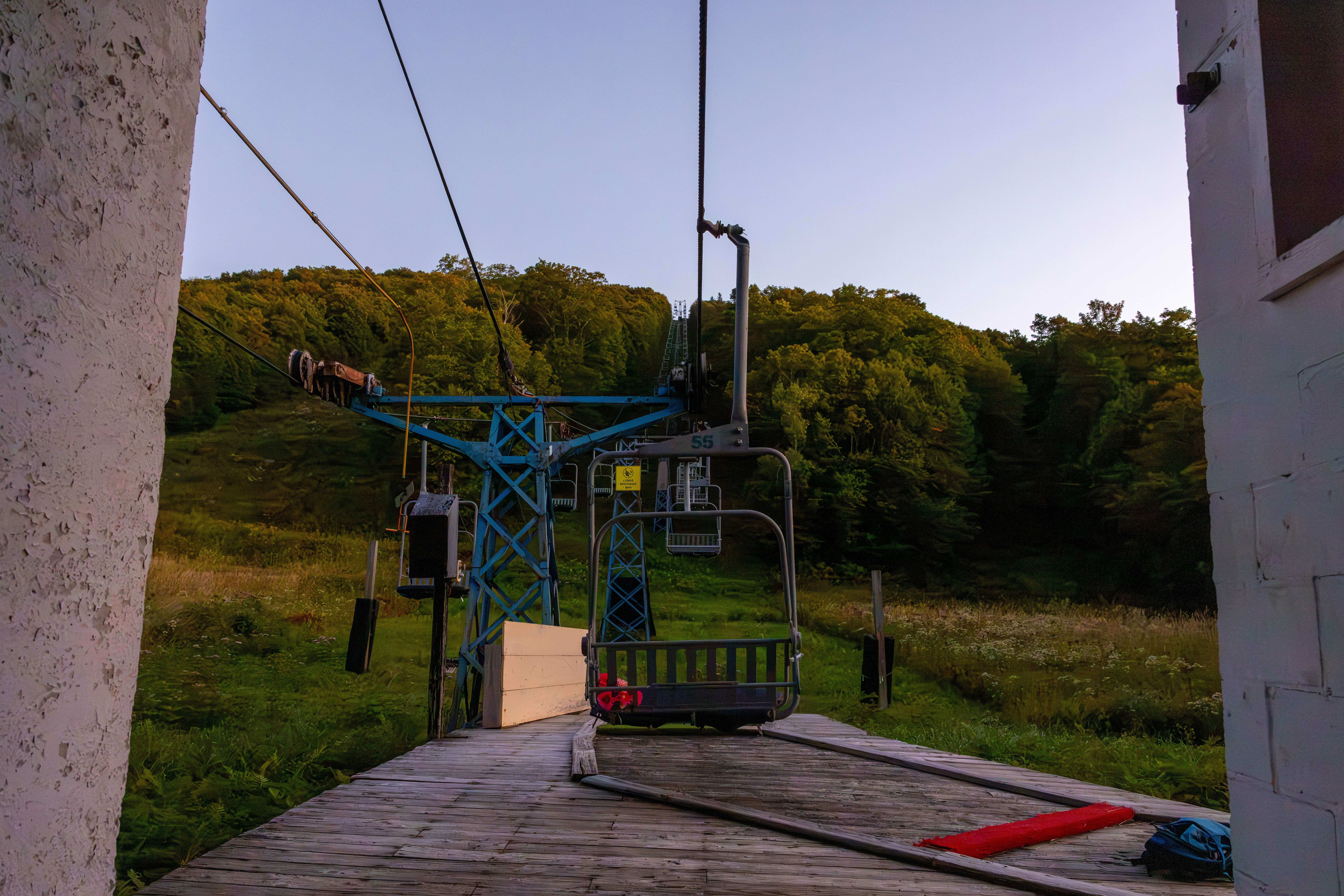 A mountain chairlift at dusk, with lush green hills in the background.