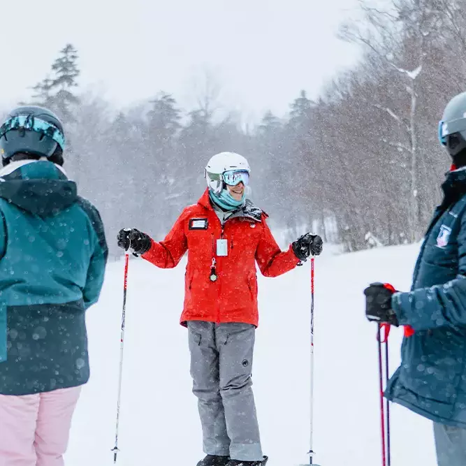 Ski instructor in red coat guides two skiers in snowy terrain on Killington Mountain.