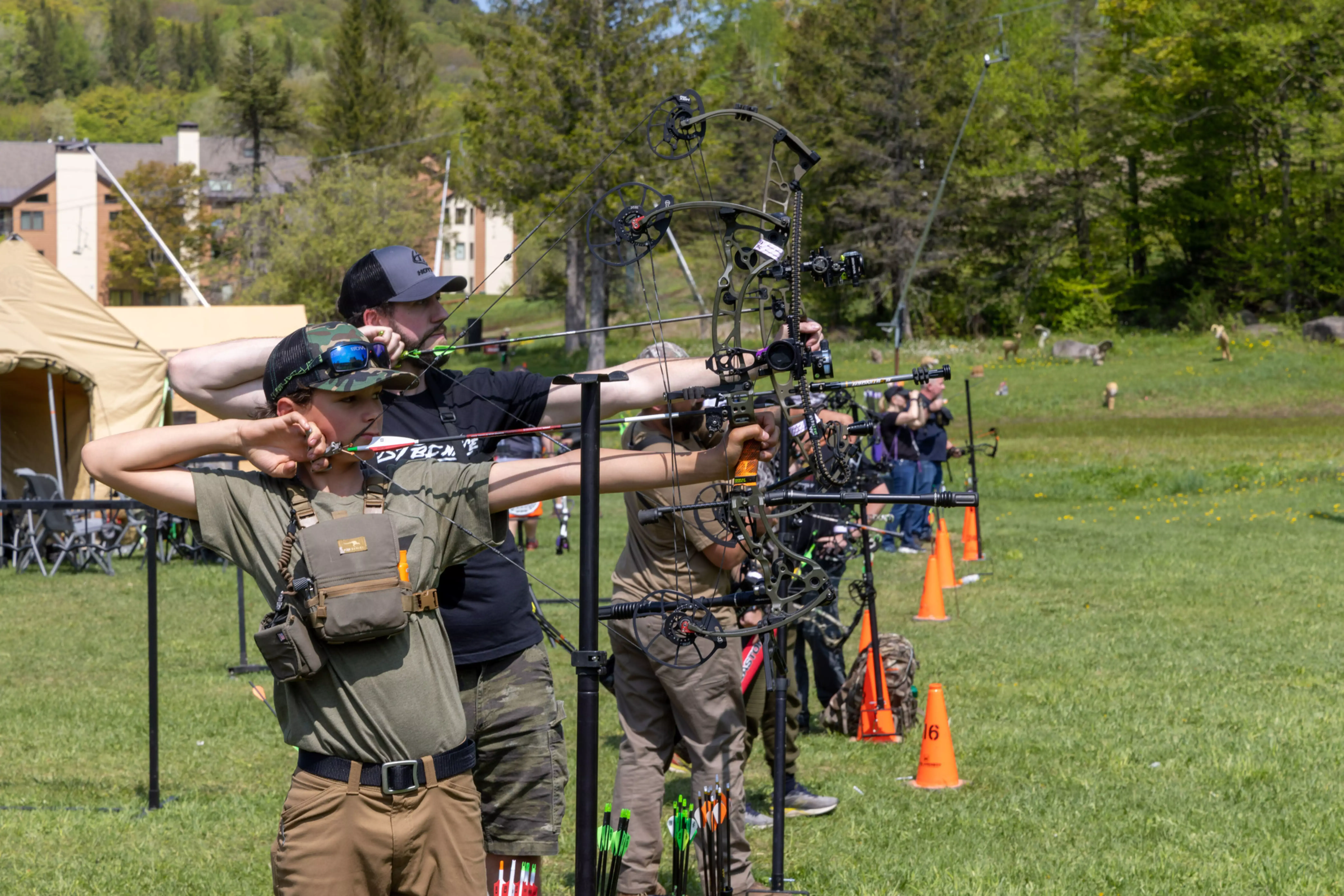 Archers in a field practicing with compound bows on a sunny day.
