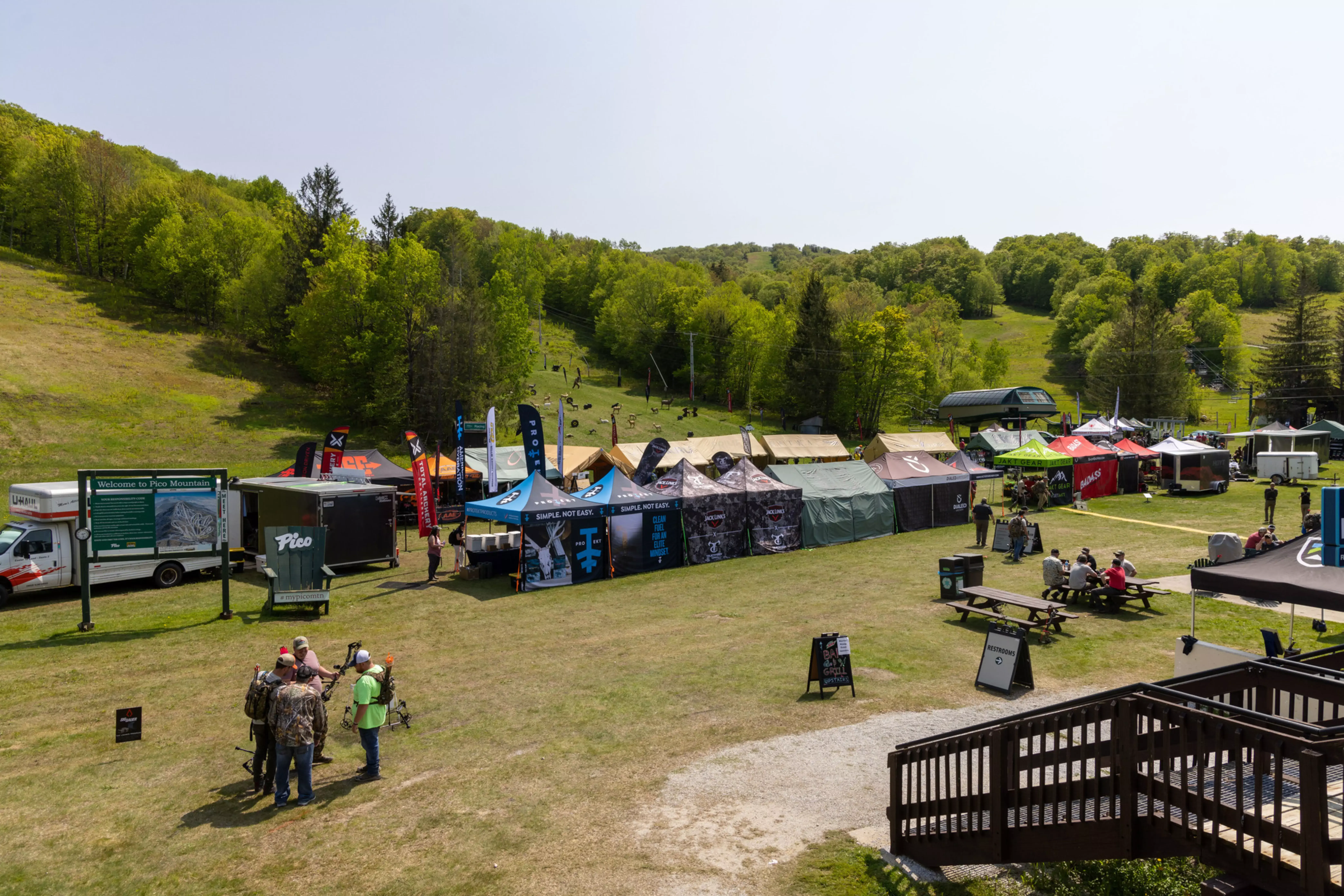 A lively outdoor event at Pico Mountain with booths, vendors, and green hills in the background.