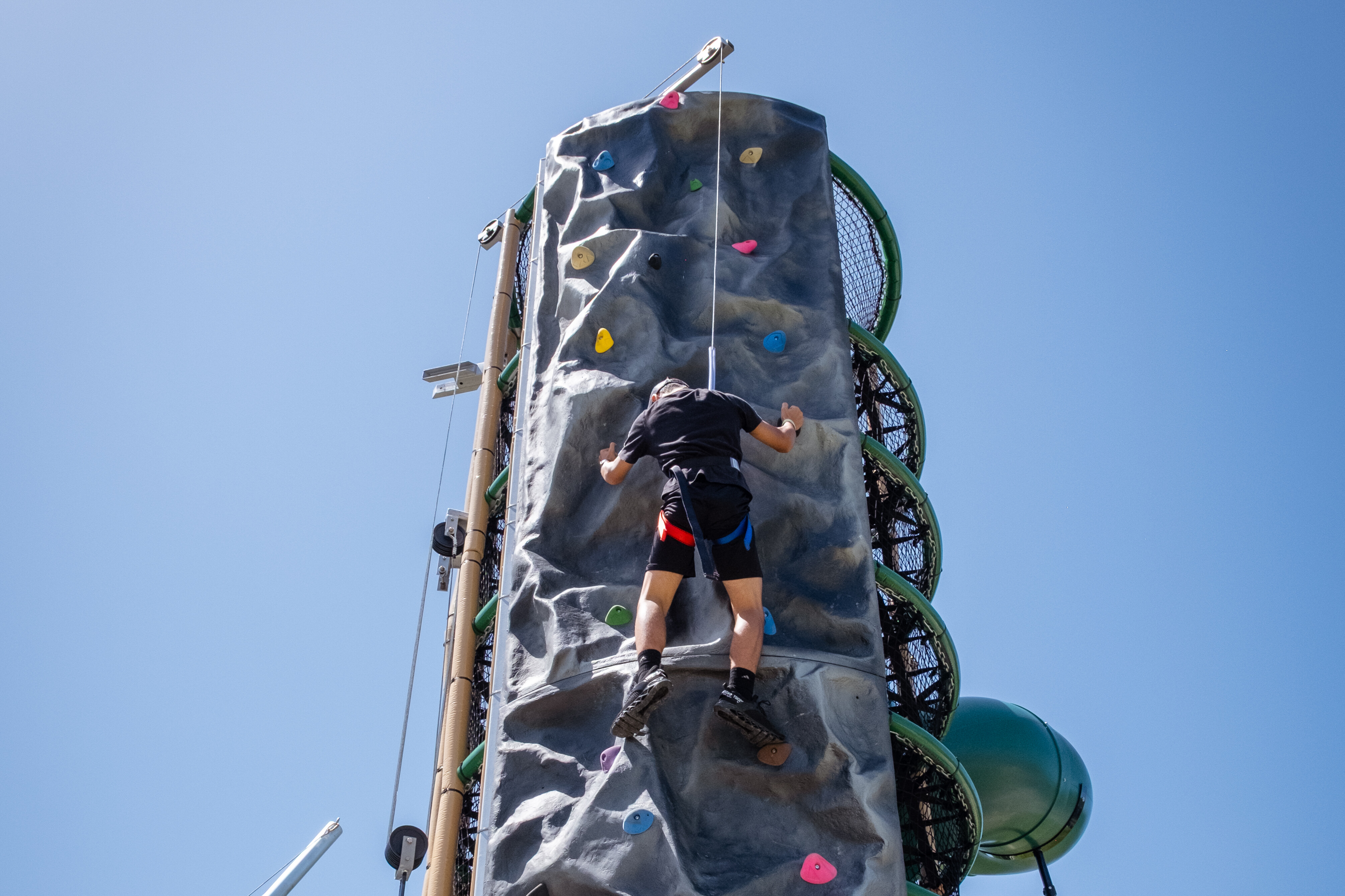 A person climbing a vertical rock wall against a clear blue sky.
