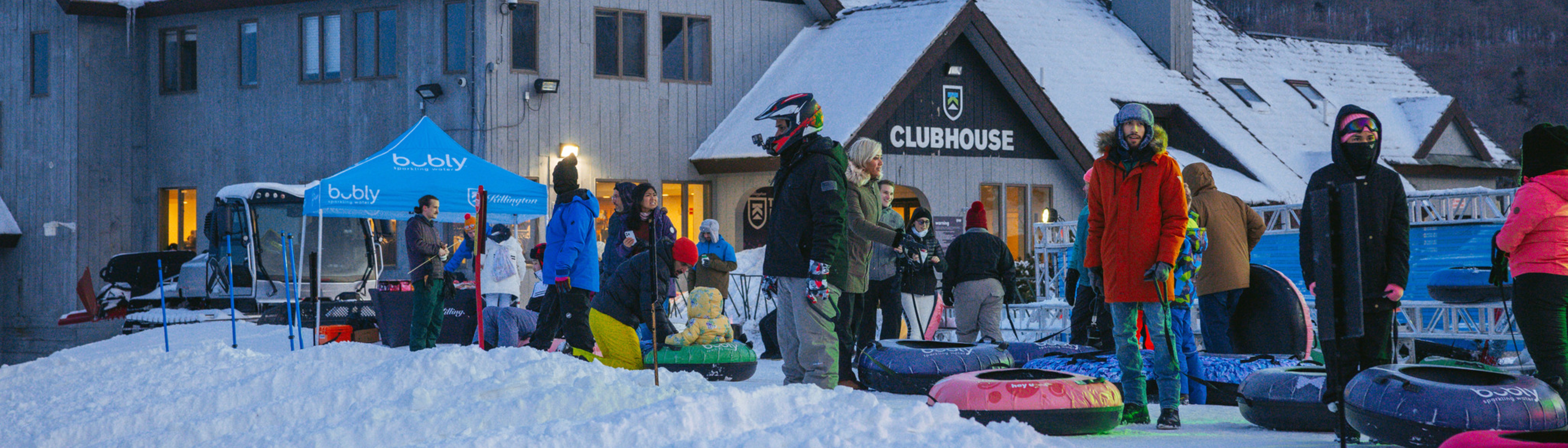 People enjoying snow tubing near a clubhouse, surrounded by snowy terrain.