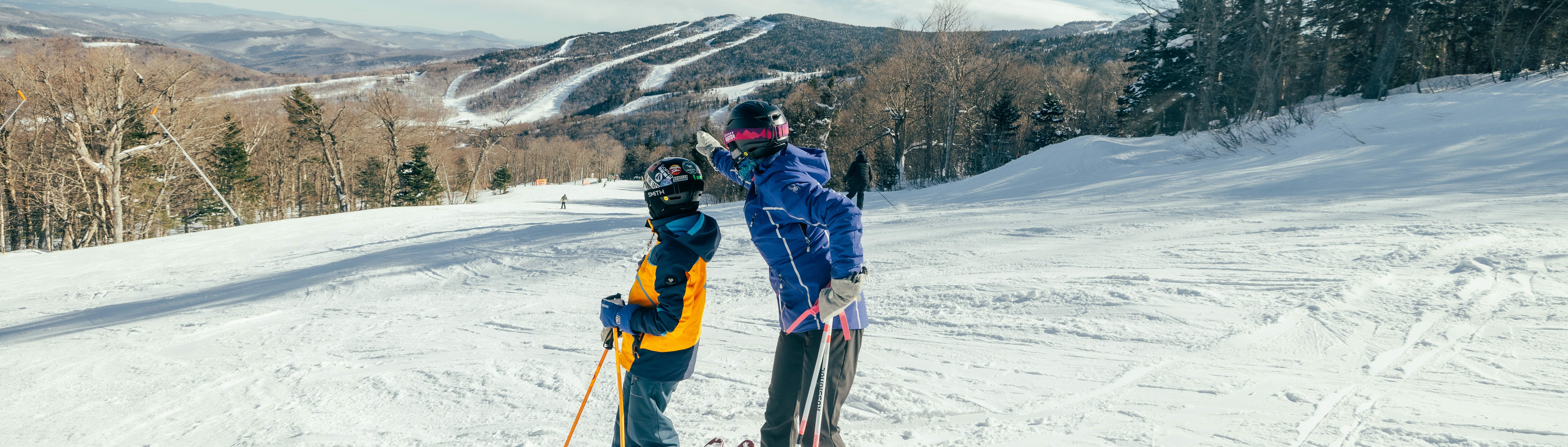 A child and adult skier pose together on a snowy mountain slope.
