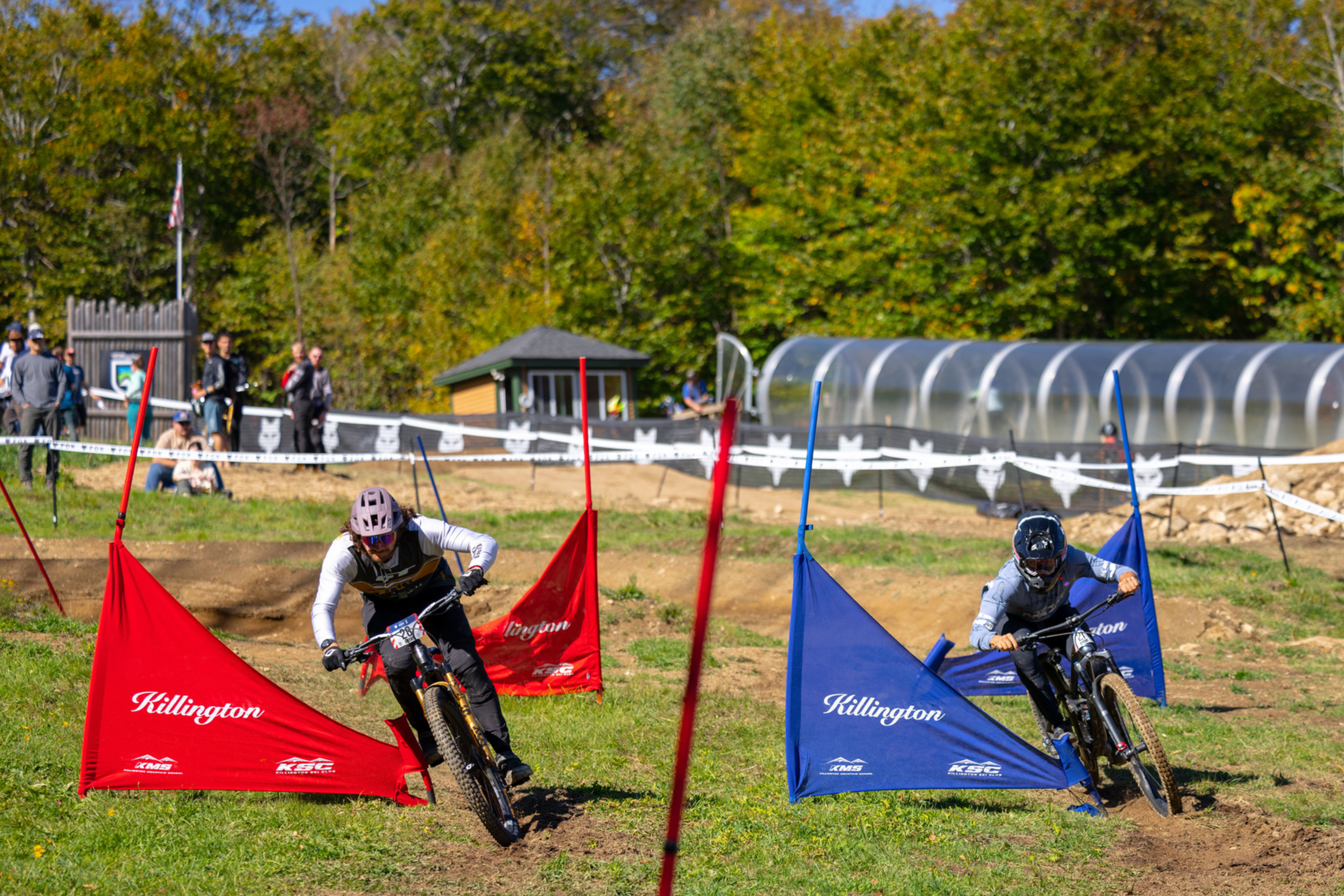 Two mountain bikers race around colorful flags on a grassy course in autumn.