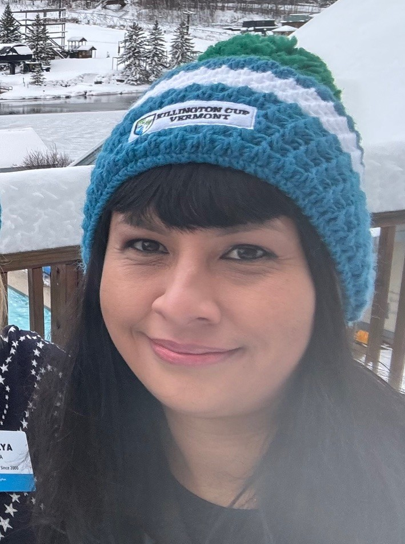Woman wearing a blue knit hat smiles in a snowy outdoor setting.