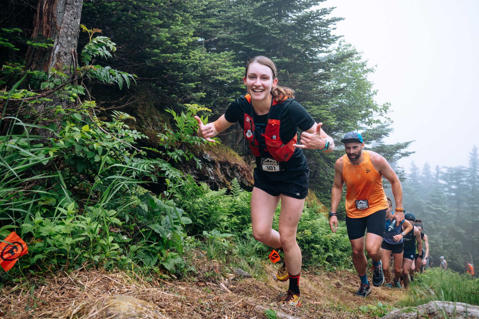 Runners ascend a misty trail, smiling and encouraging each other amid lush greenery.