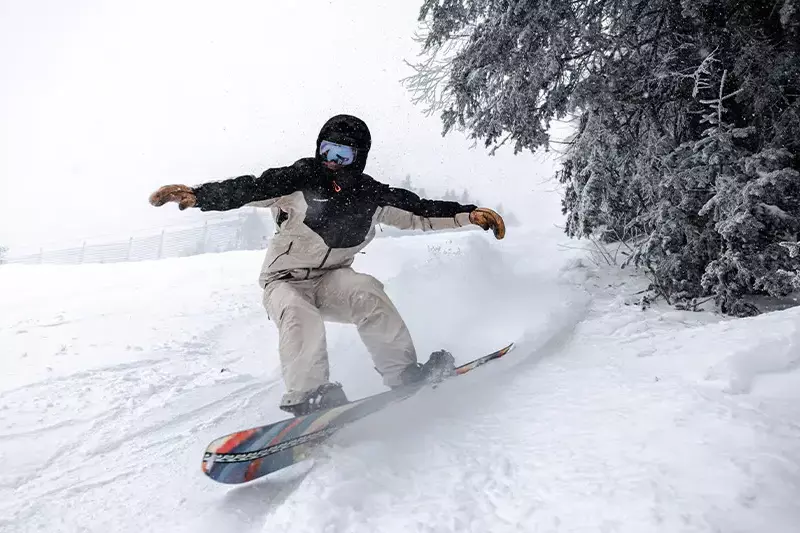 Snowboarder carving through fresh snow in a winter landscape.