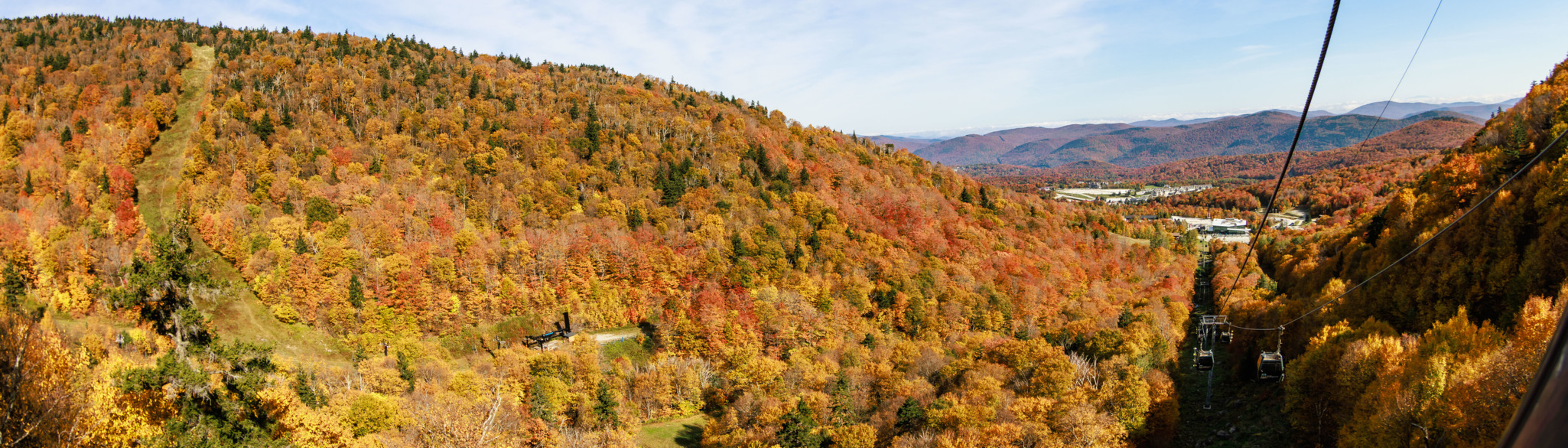 Vibrant autumn foliage covers rolling hills under a clear blue sky.