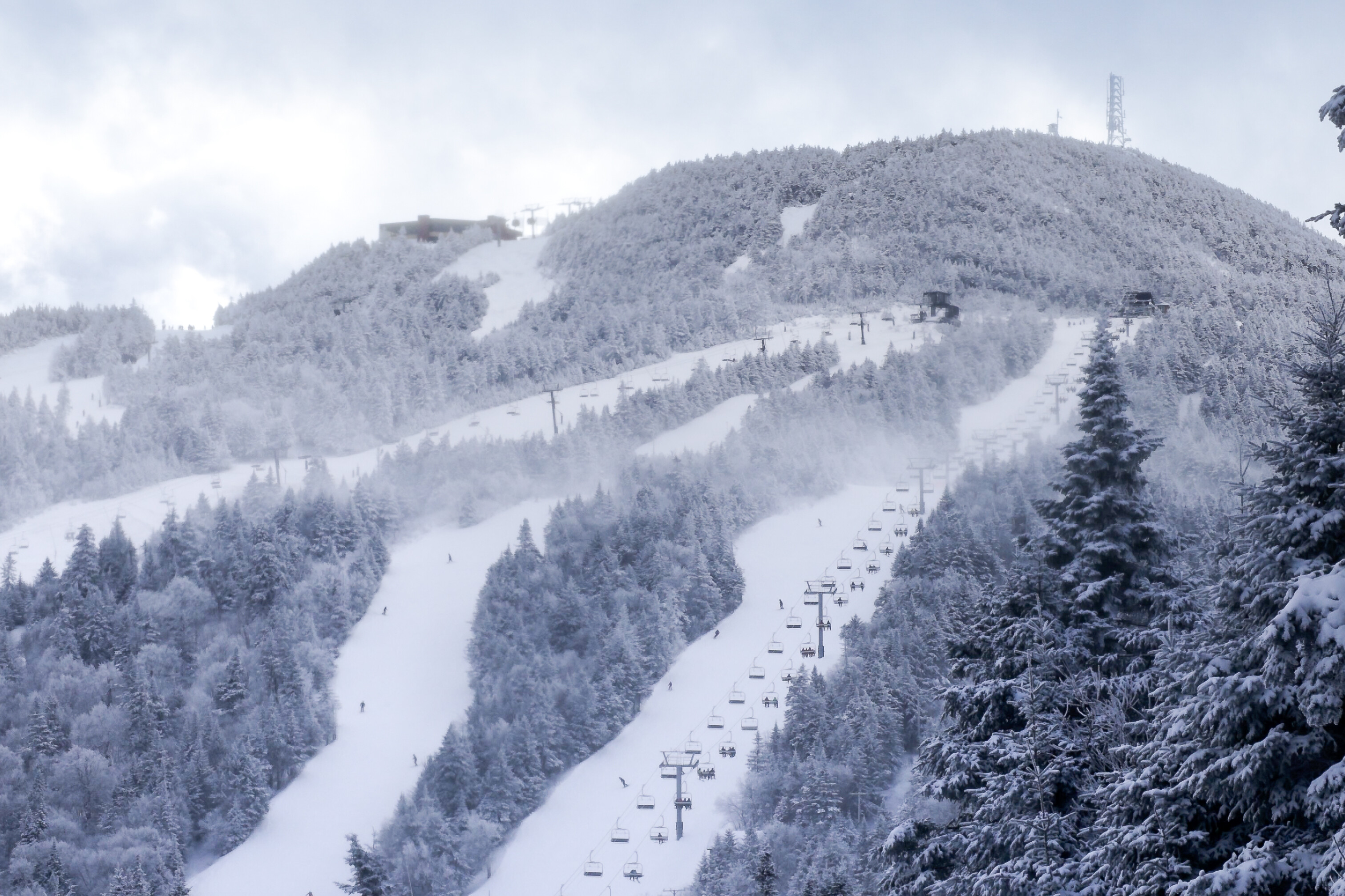 Snow-covered mountain slope with ski lifts and trees, under a cloudy sky.