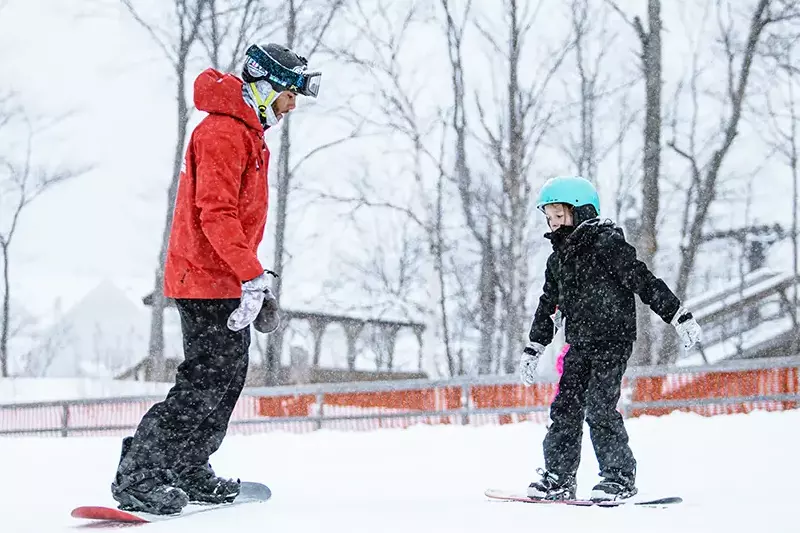 A snowboarding instructor teaches a child in a snowy landscape.