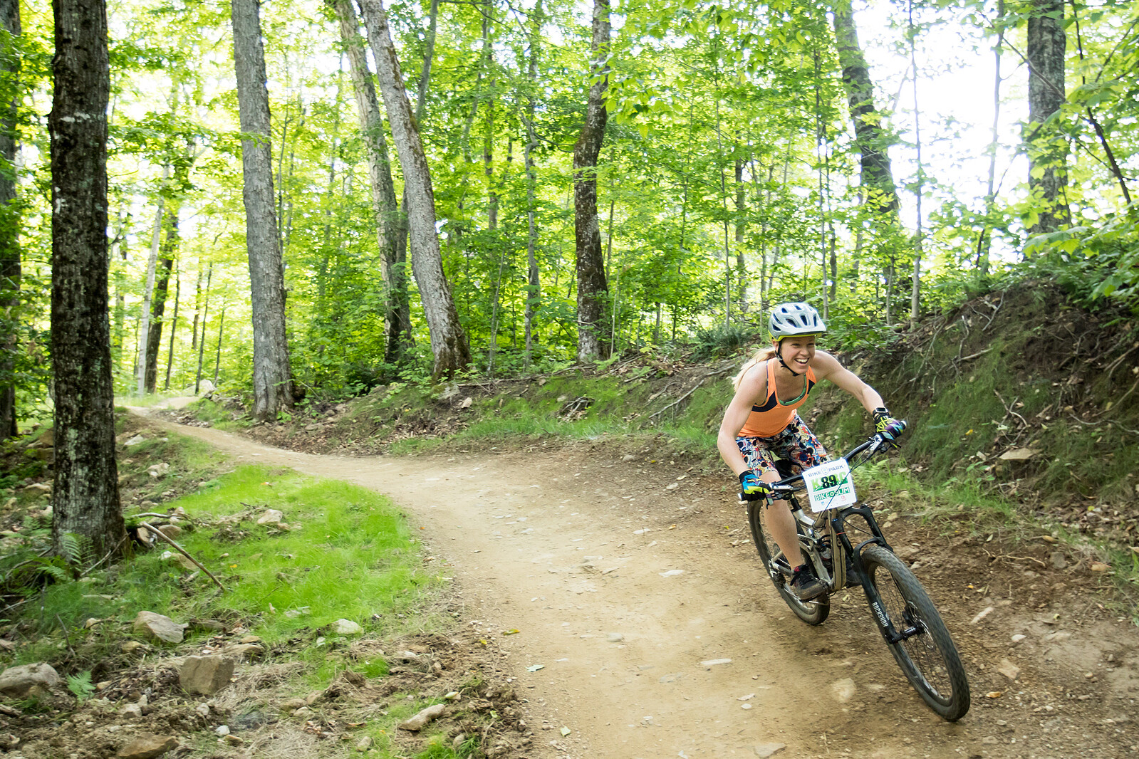 A woman enjoys mountain biking on a dirt trail in a lush green forest.