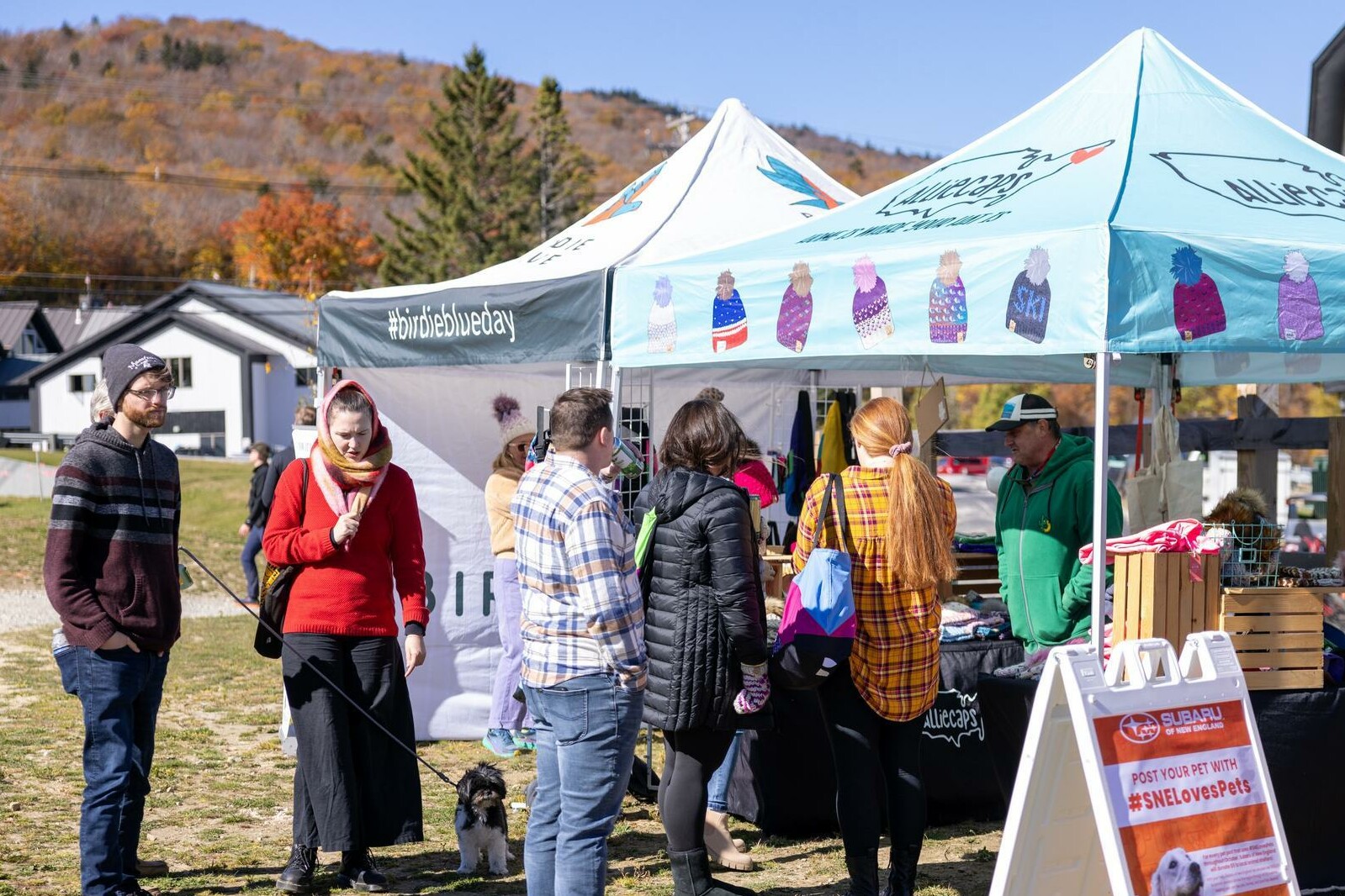 People browsing a market stall with colorful hats in a fall outdoor setting.
