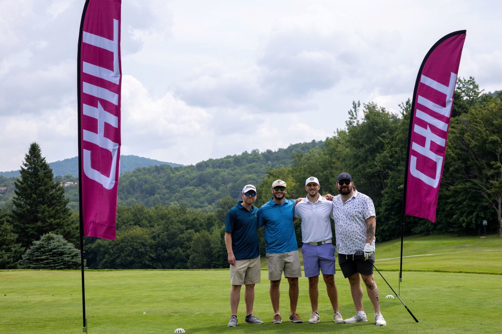 Four friends posing for a photo on a golf course beside a "CHILL" flag.