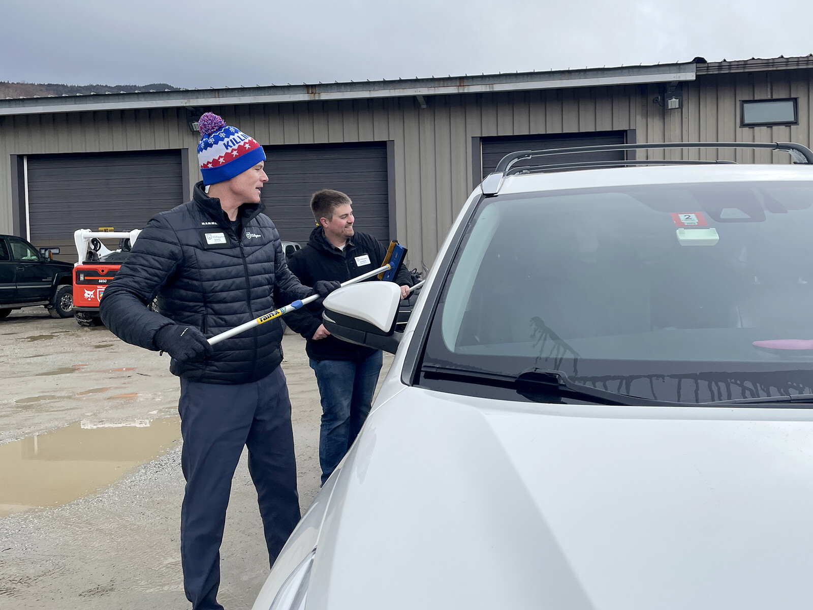 Two men washing cars in a parking lot, wearing winter clothing.