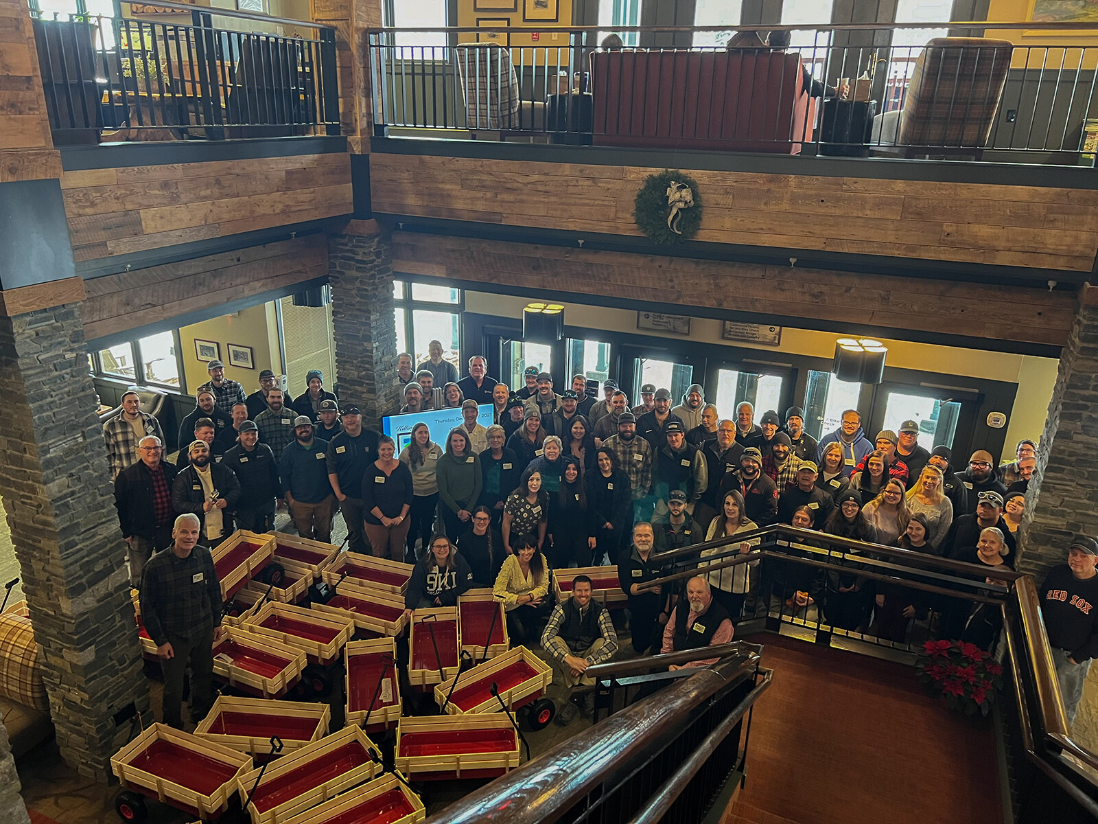 Group photo of a large gathering indoors with wooden wagons in front.