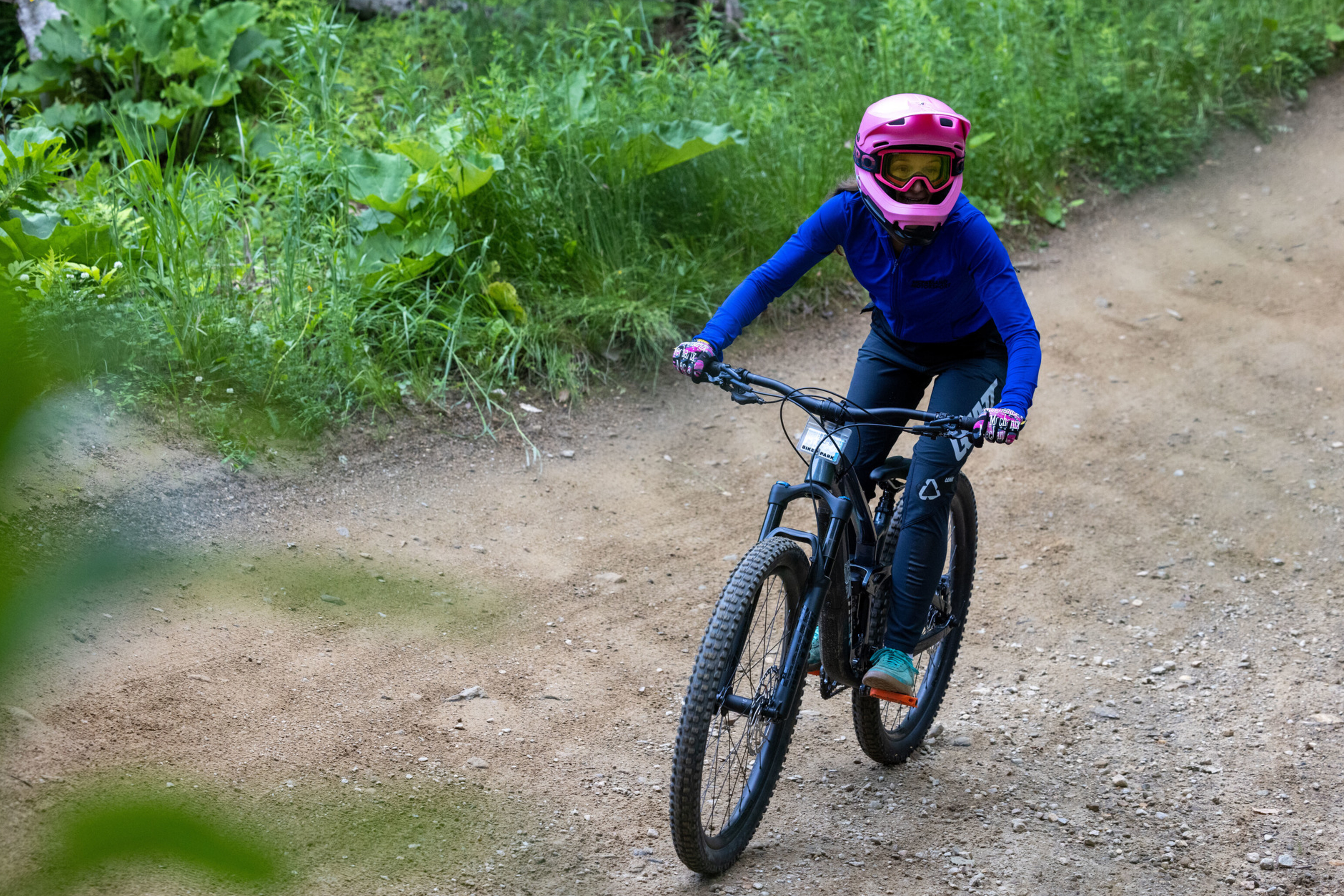 A cyclist in a pink helmet rides on a gravel path surrounded by greenery.