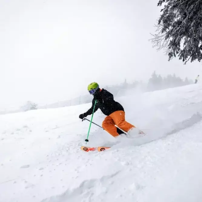 Person skiing down a snowy slope in bright orange pants and a green helmet at Killington Mountain.