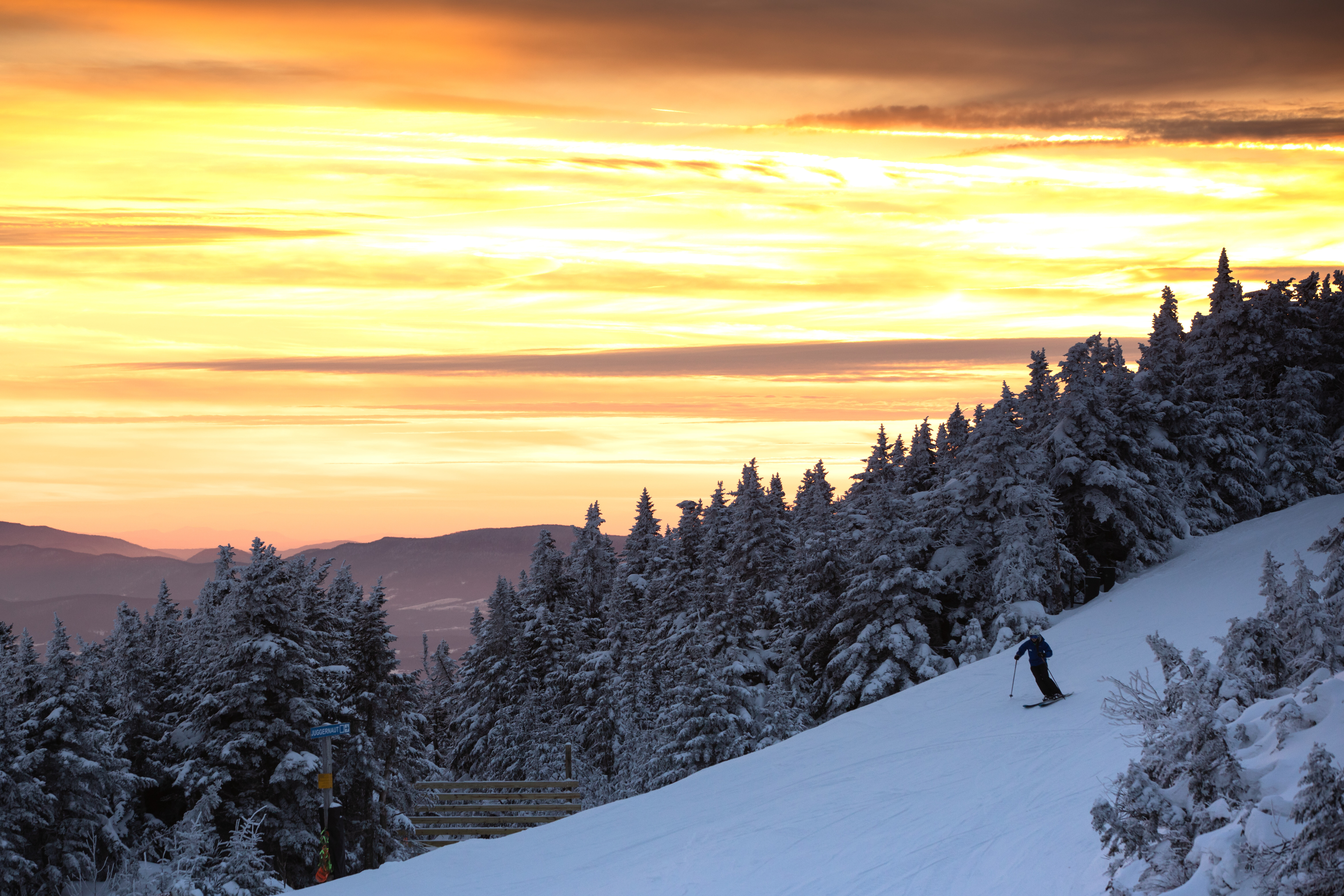 Skier on a snowy slope under a vibrant sunset and frosted trees.