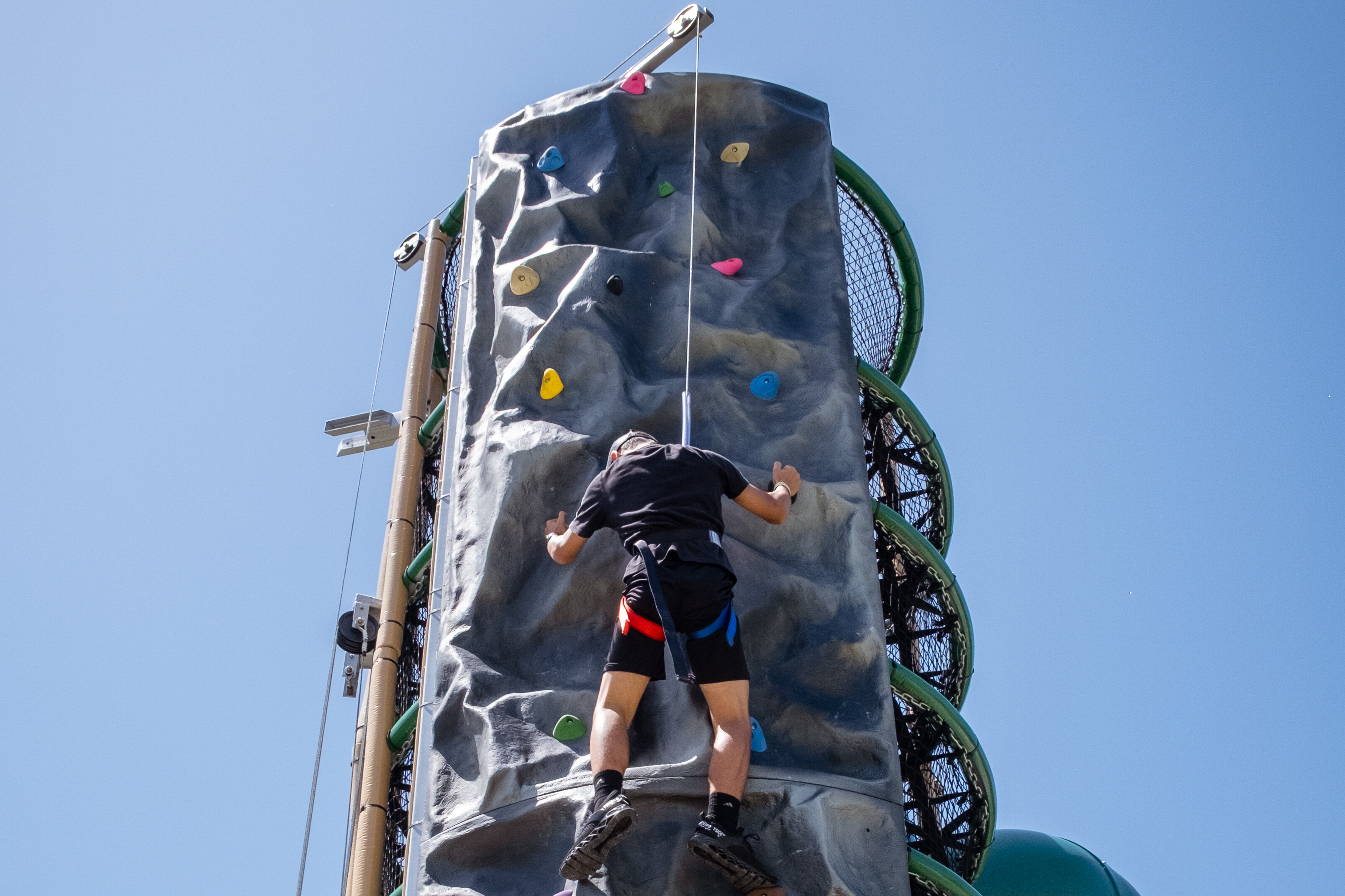 Child climbing a rock wall under a clear blue sky.