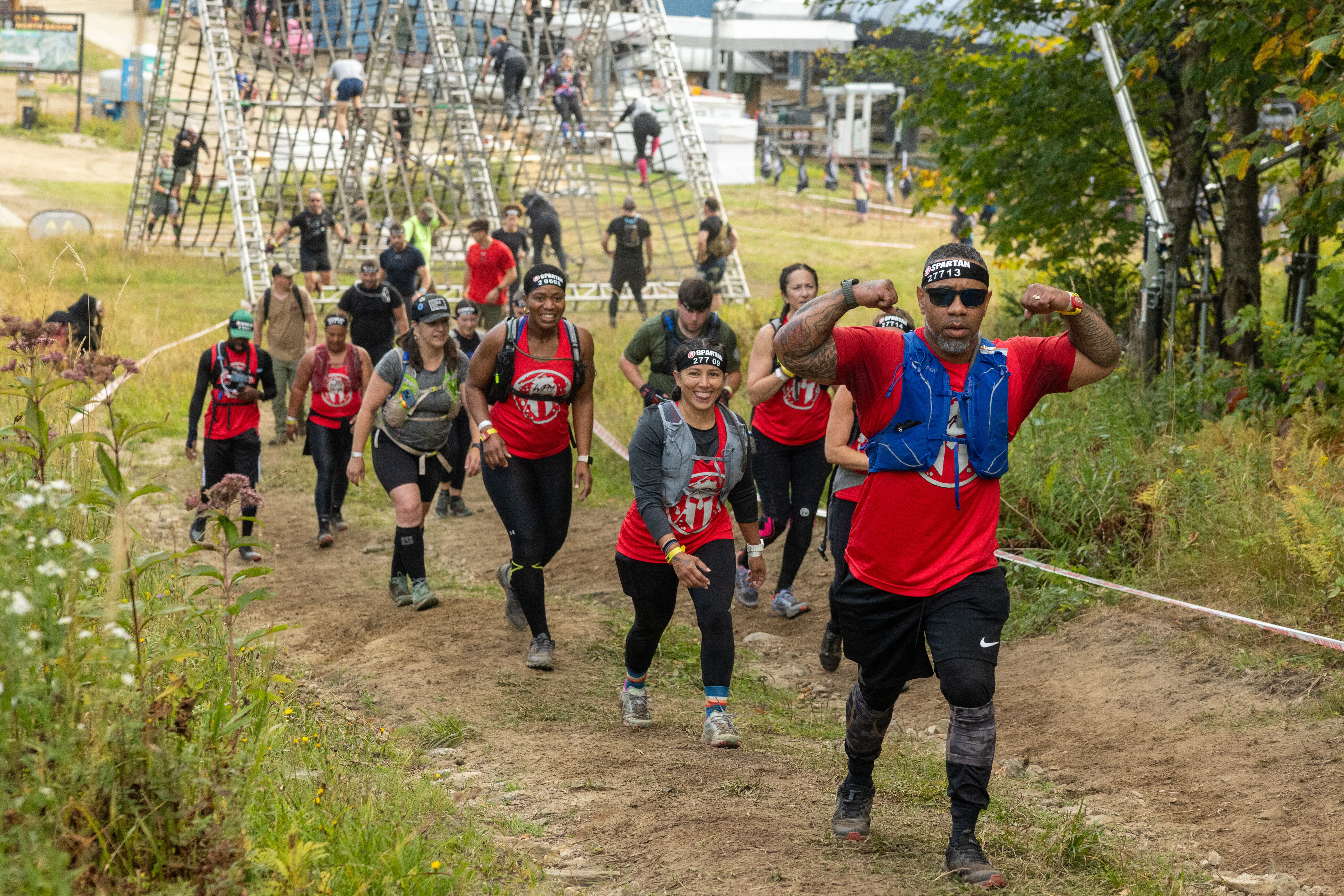 A group of runners in red shirts competing in an obstacle race on a dirt path.