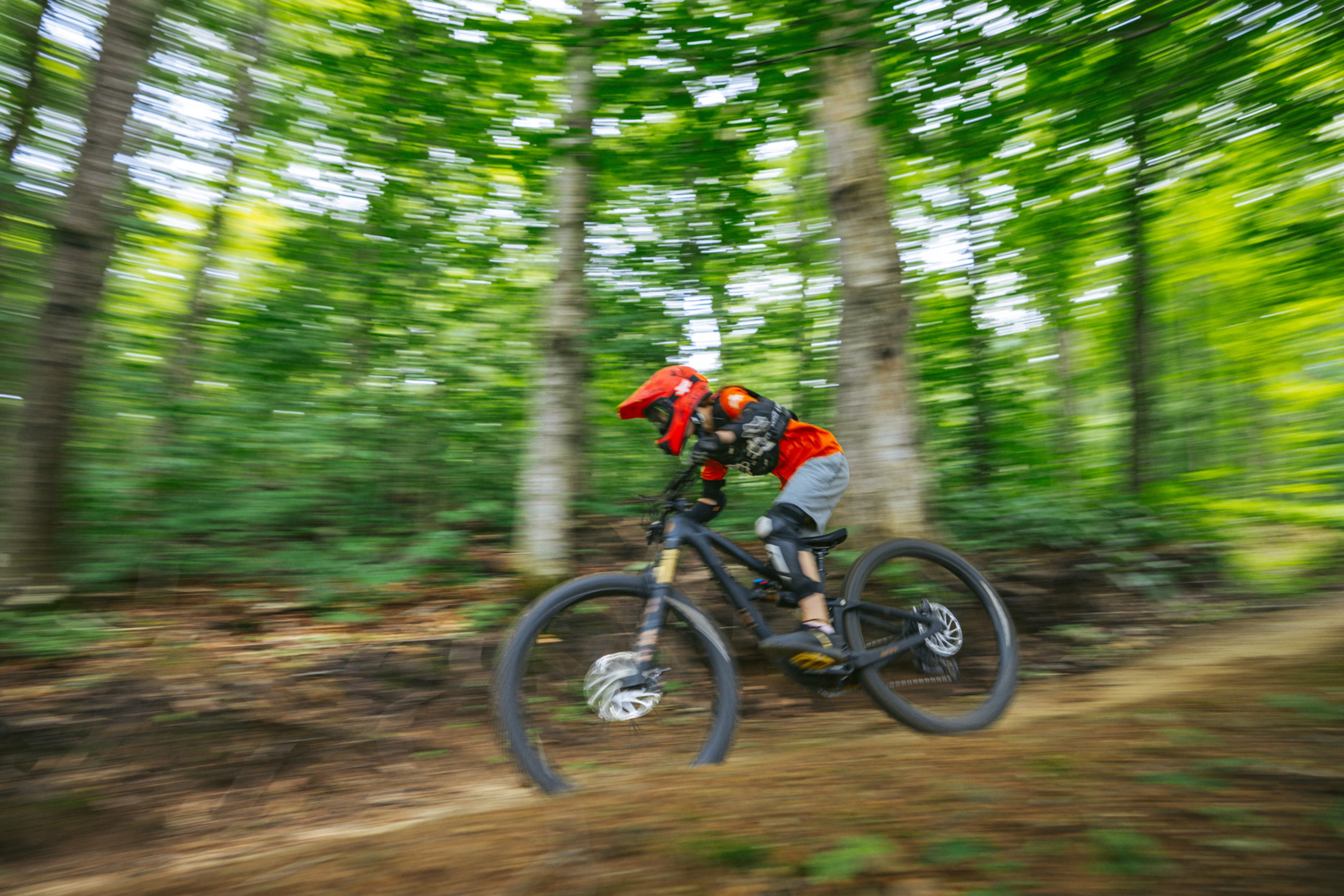 A mountain biker in motion rides through a lush, forested trail.